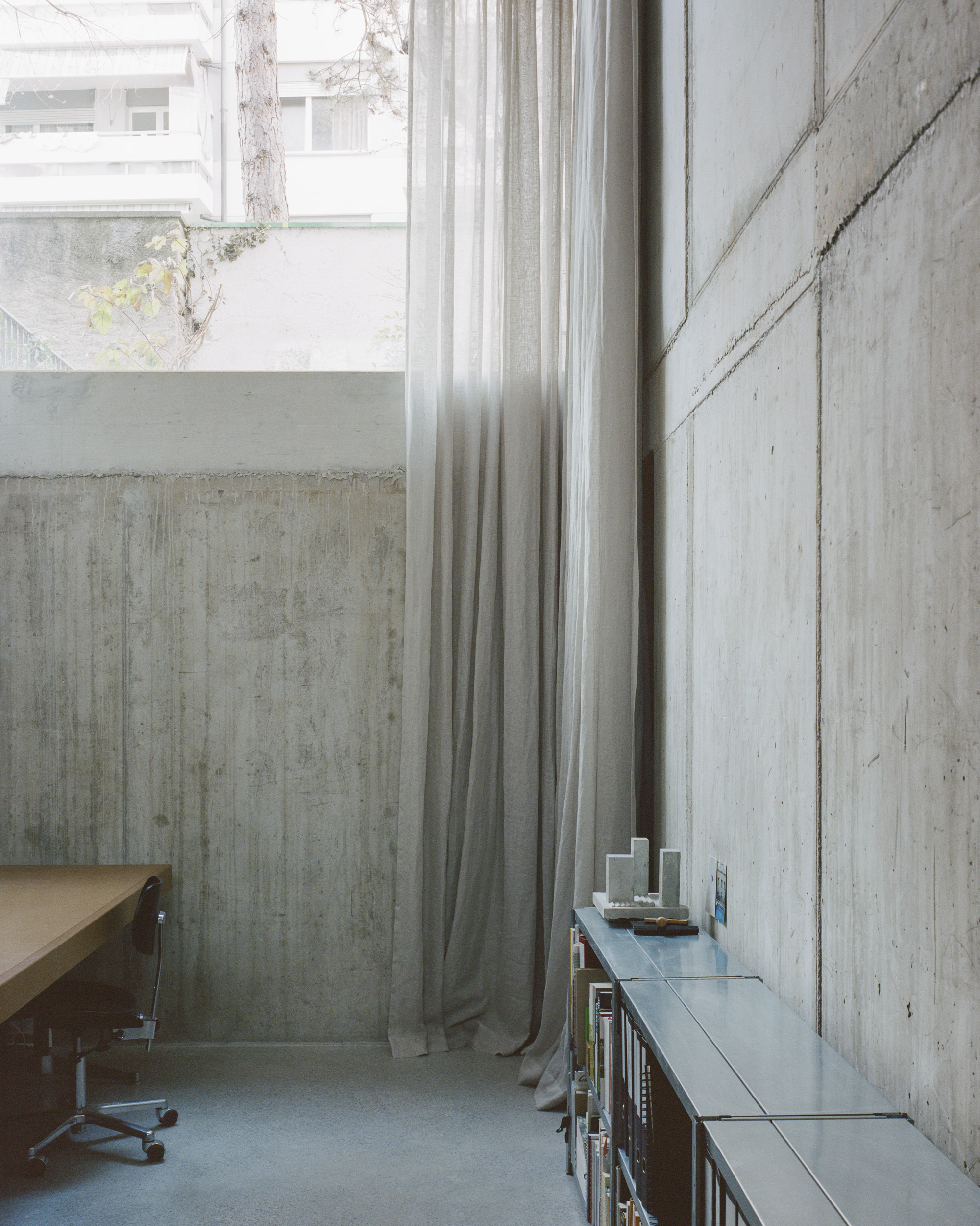 Concrete wall panels with floor-to-ceiling linen curtain beside a narrow office desk