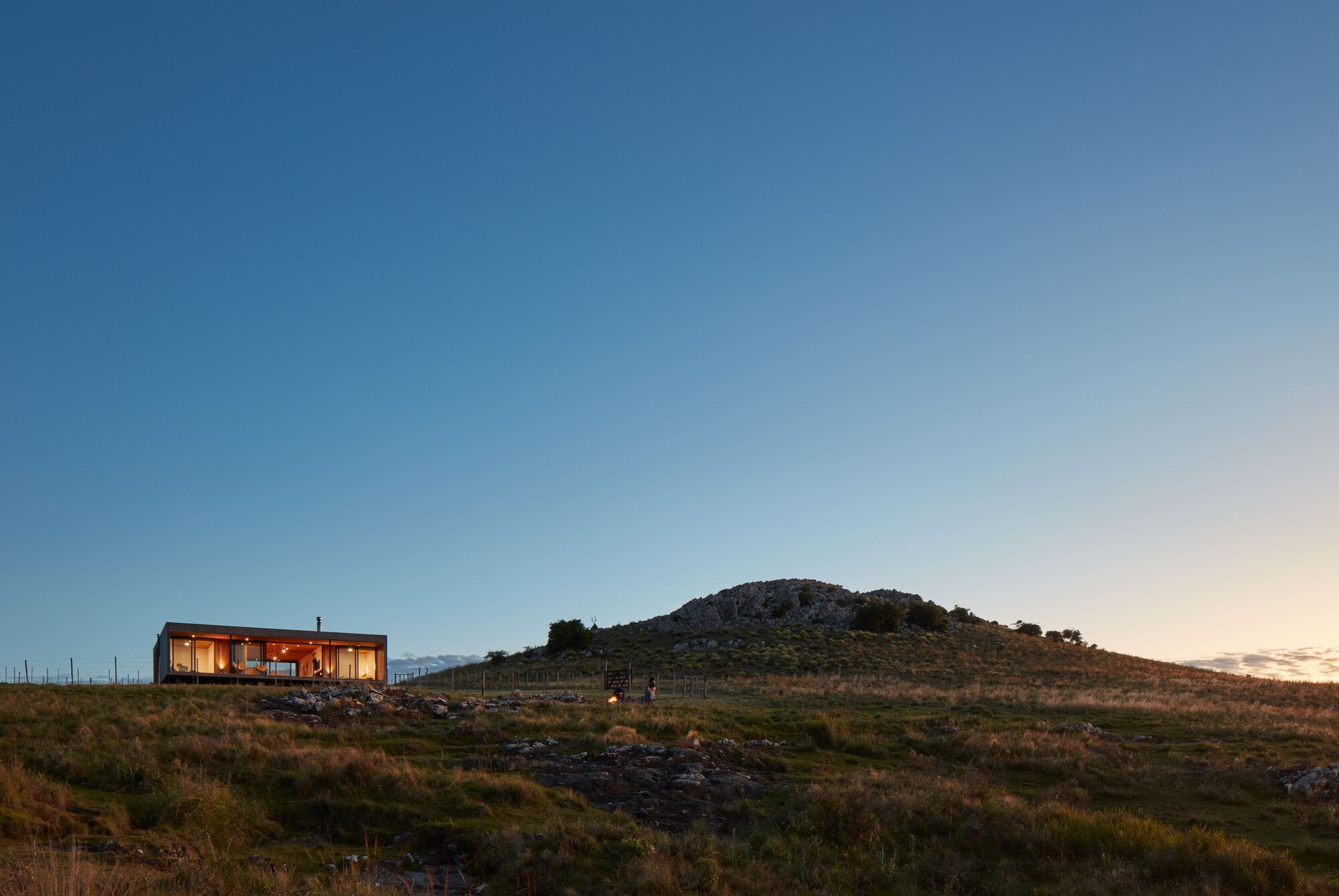 Long view of the illuminated glass volume on a hillside at twilight