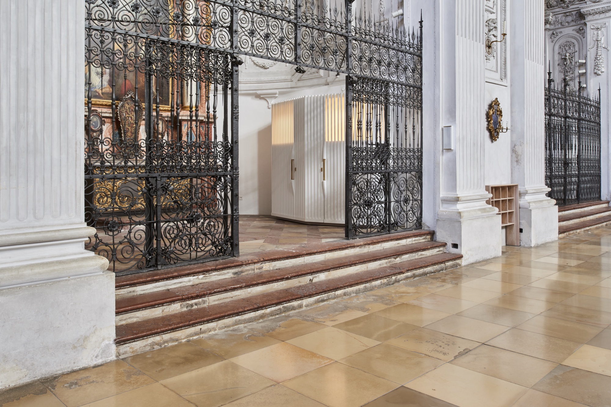 Low marble steps leading up to the wrought iron enclosure with vertical ribbed timber volumes beyond