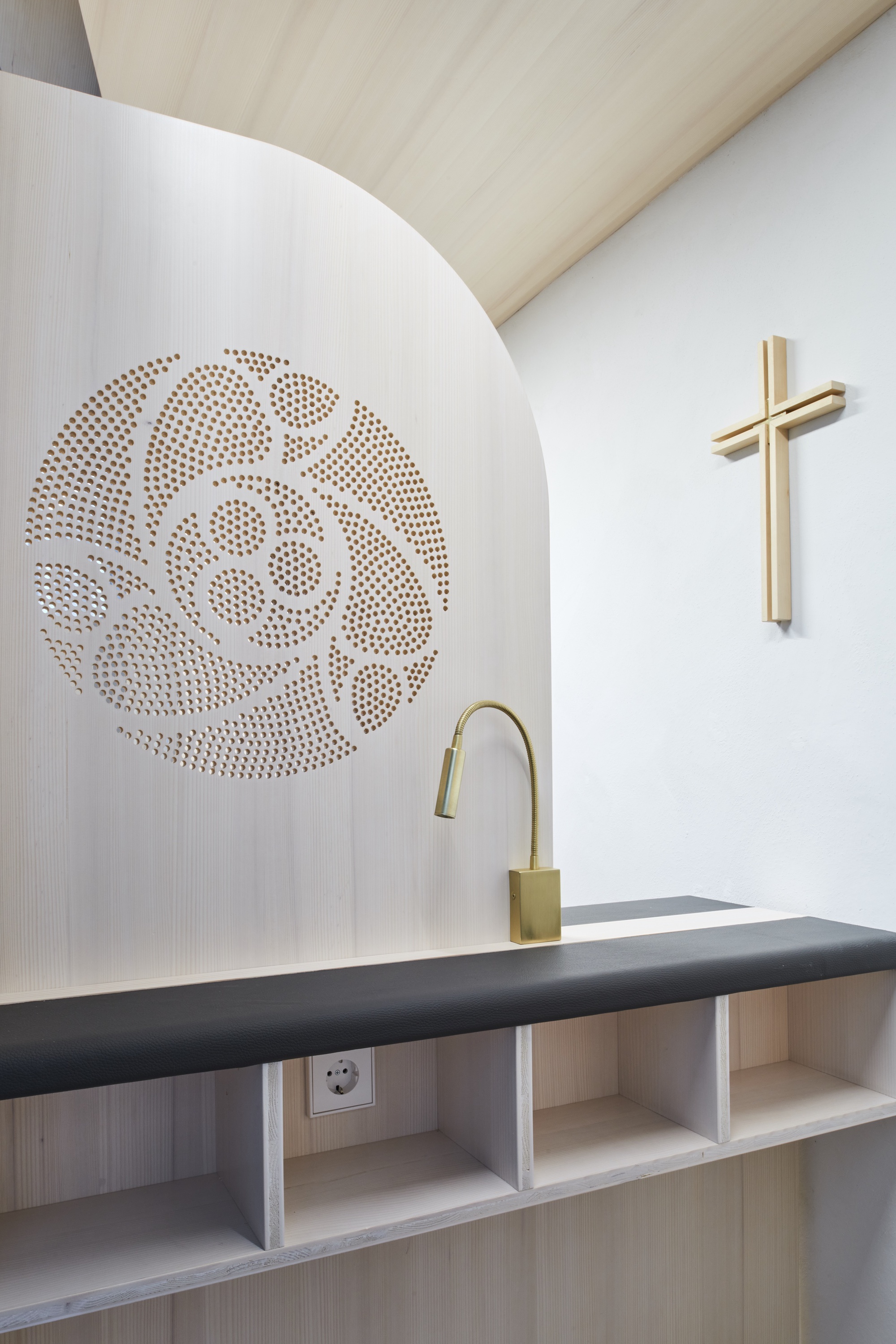 Close-up of the perforated white panel with decorative circular pattern above a dark upholstered bench and brass faucet