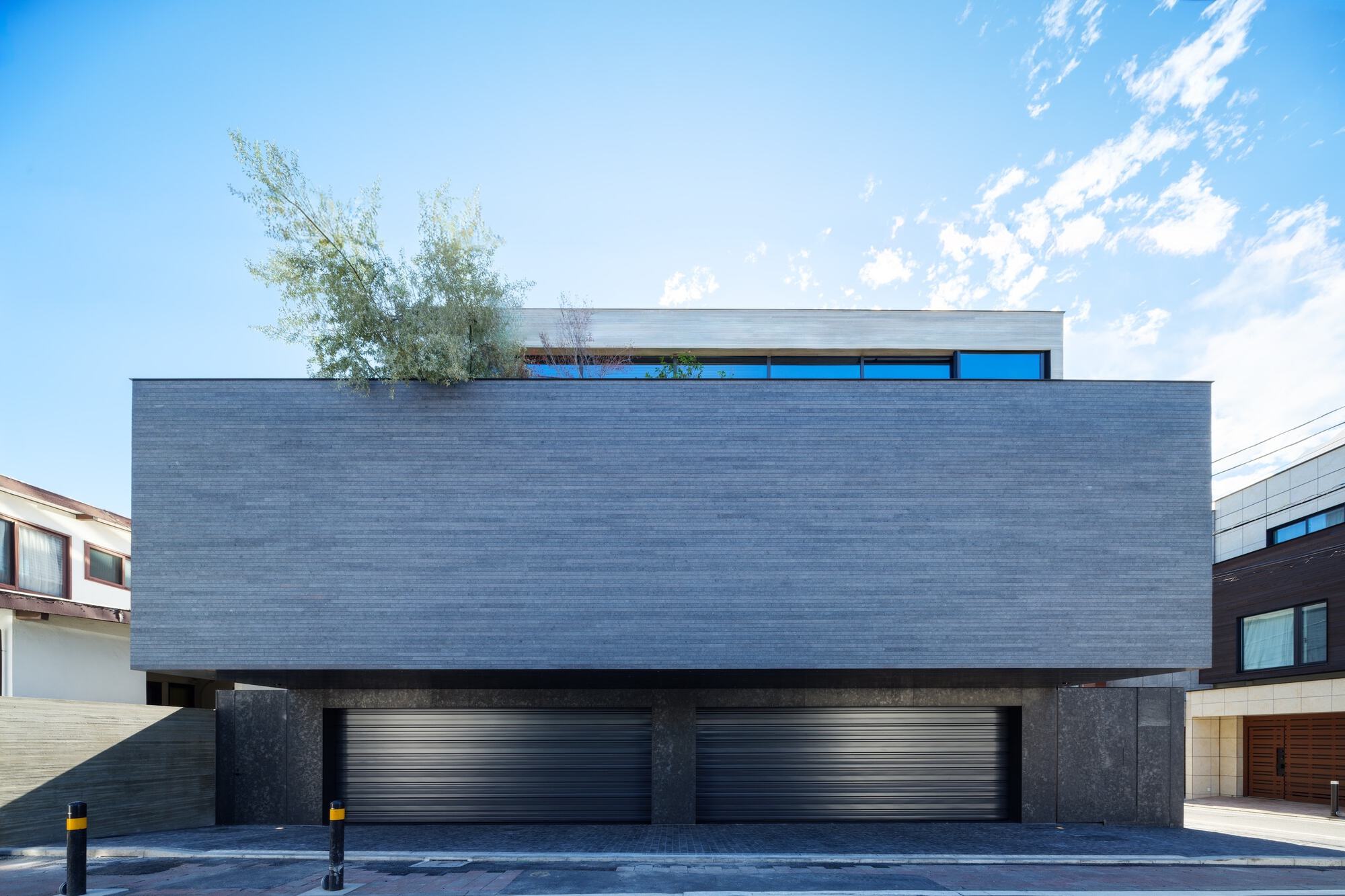 Street elevation with dark brick facade cantilevered over double garage doors beneath clear blue sky