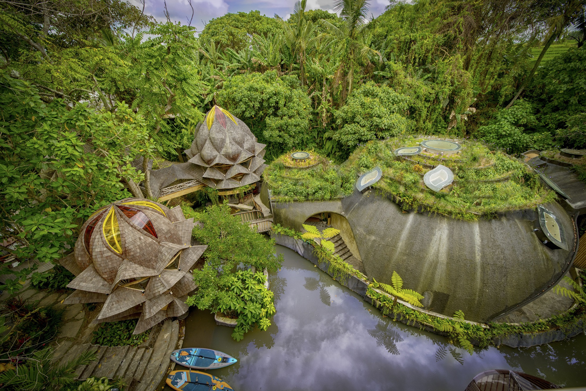 Aerial view of planted roofs forming curved organic shapes around reflecting pools in dense jungle vegetation