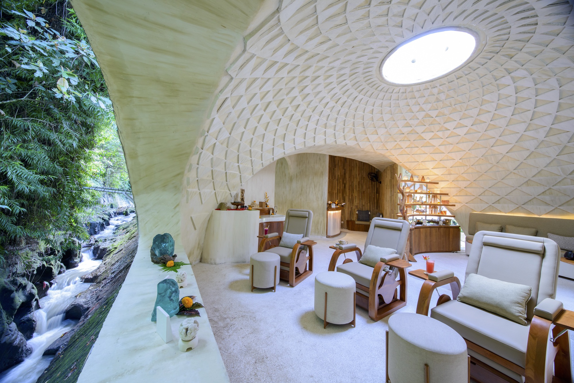 Vaulted interior with woven bamboo ceiling and central oculus opening to waterfall and jungle beyond