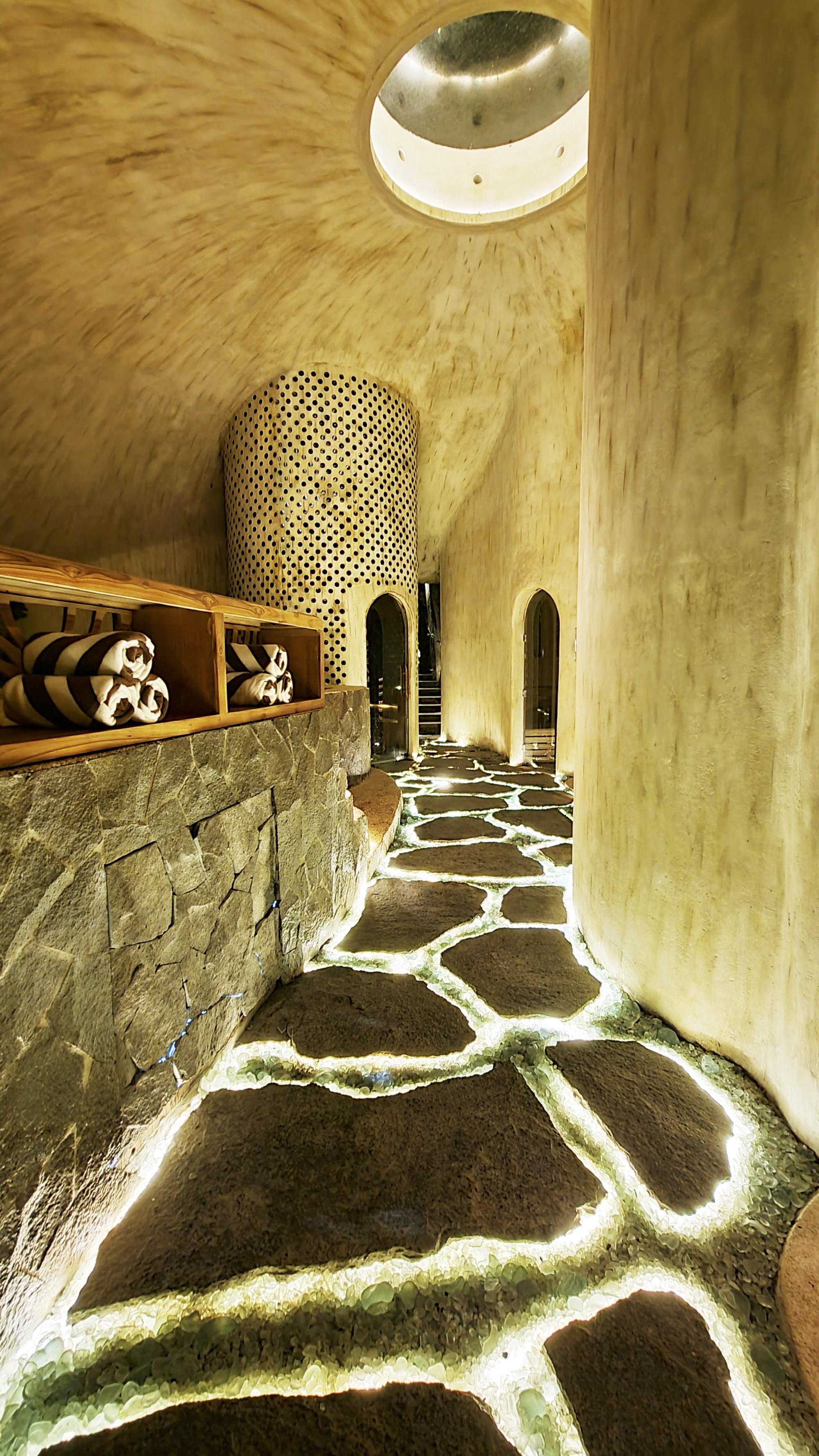 Corridor with irregular stone floor joints and perforated bamboo cylinder beneath a circular skylight