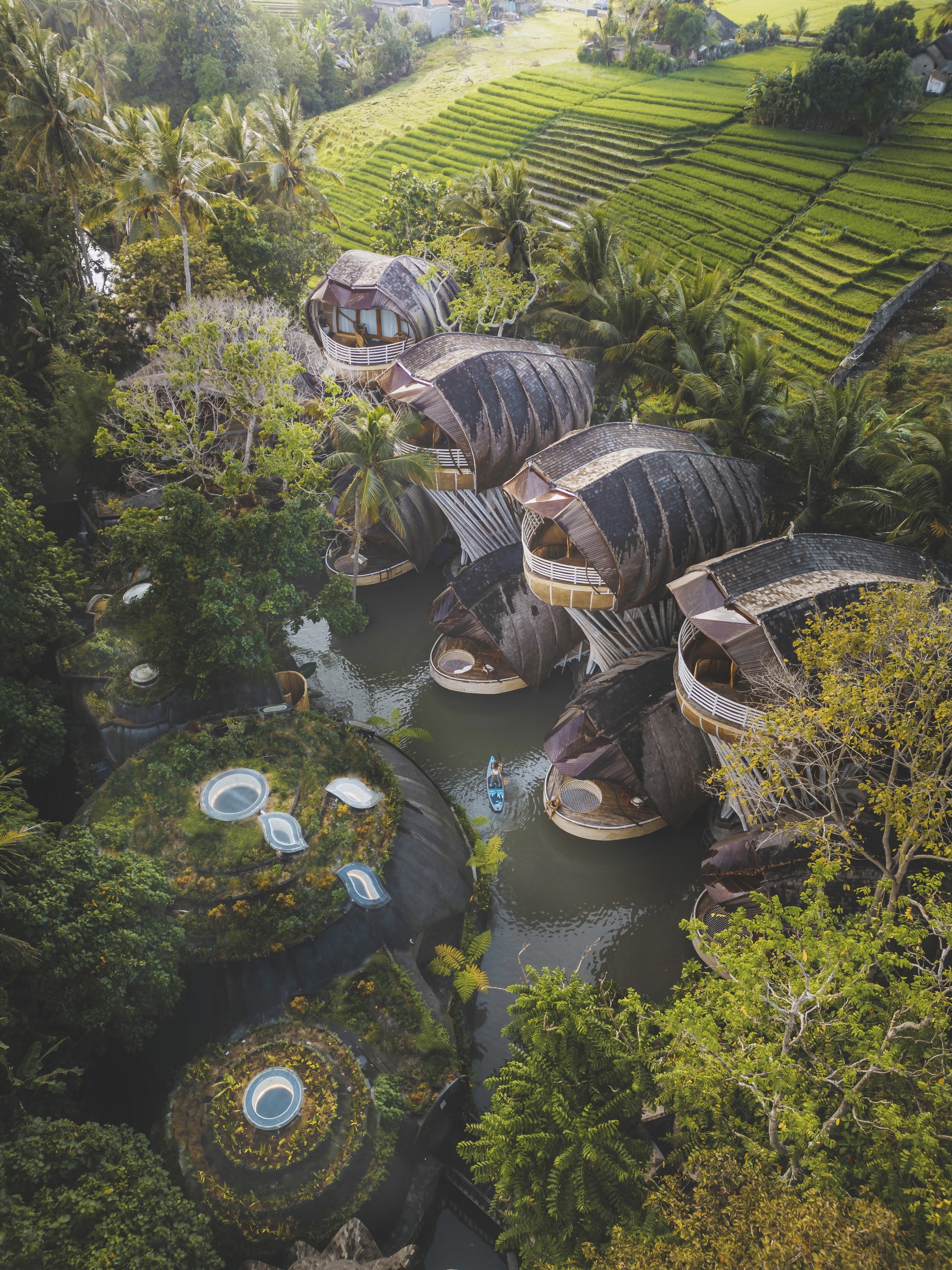 Aerial view of ribbed barrel-vault structures nestled among tropical gardens and terraced rice paddies