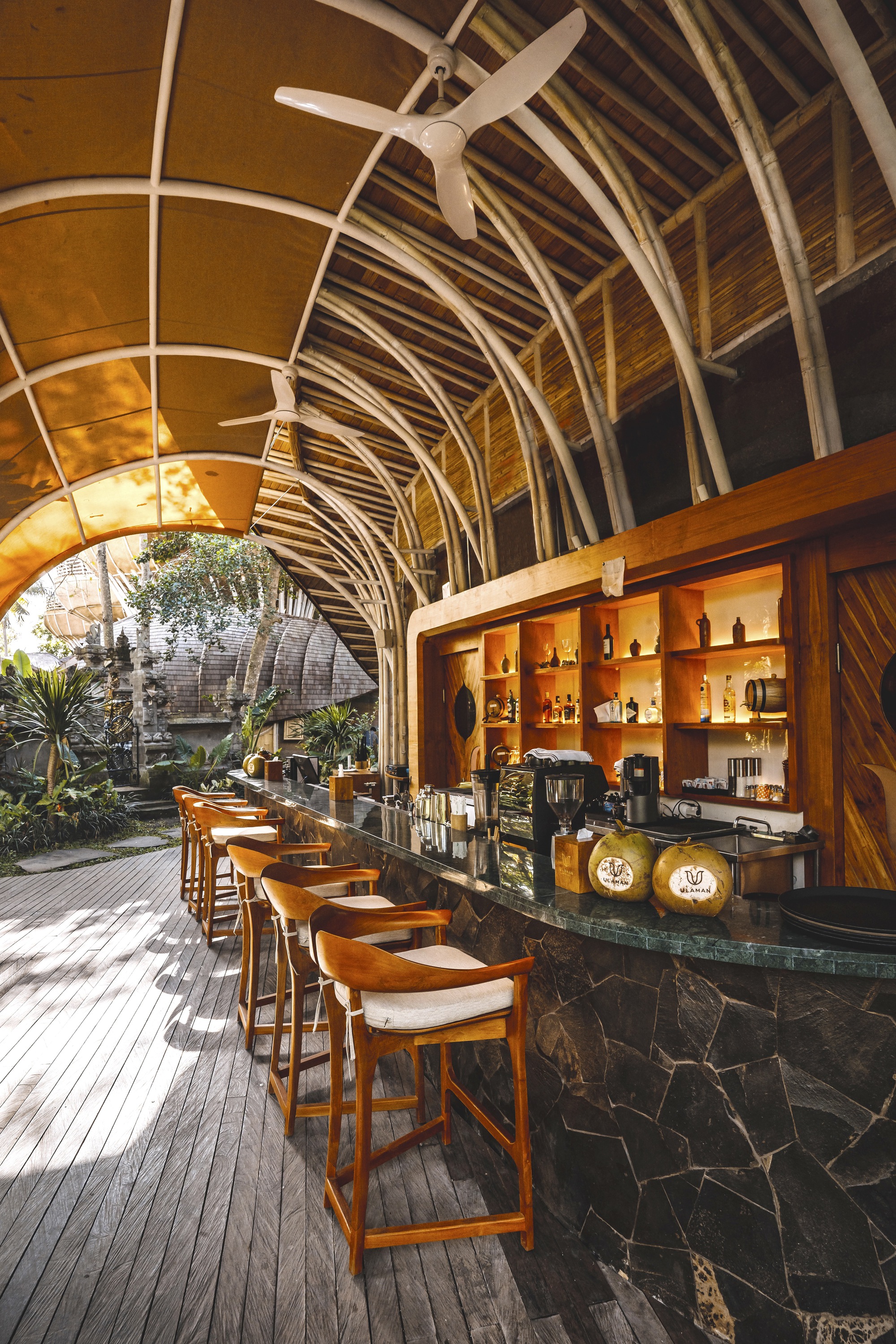 Interior bar with dark stone counter under arched bamboo ribs and exposed ceiling fan
