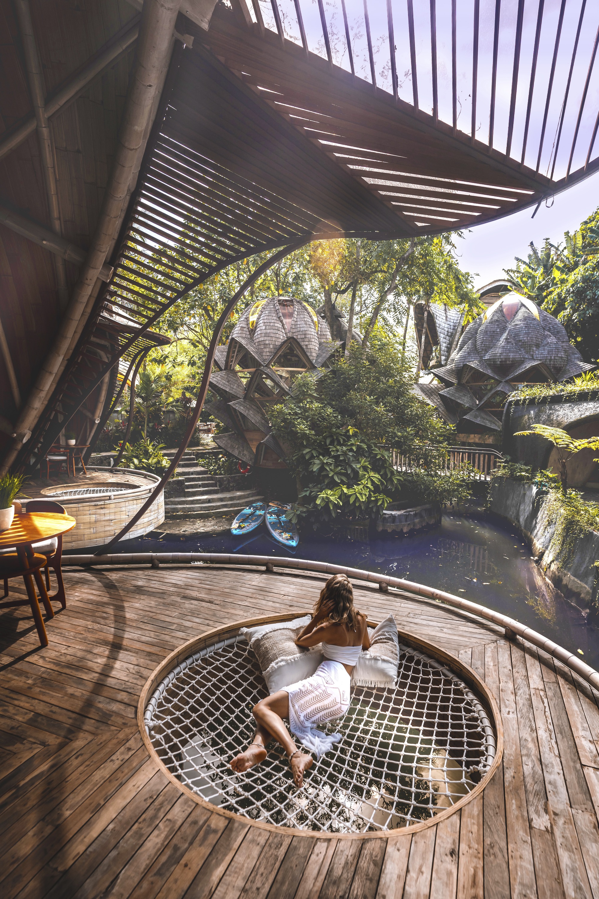 Deck with circular mesh net opening overlooking pond under slatted bamboo canopy