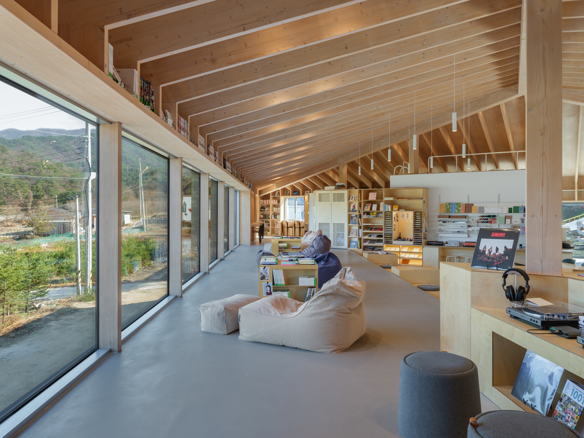 Long interior view showing exposed wood structure, glazed walls, and seating area with low tables