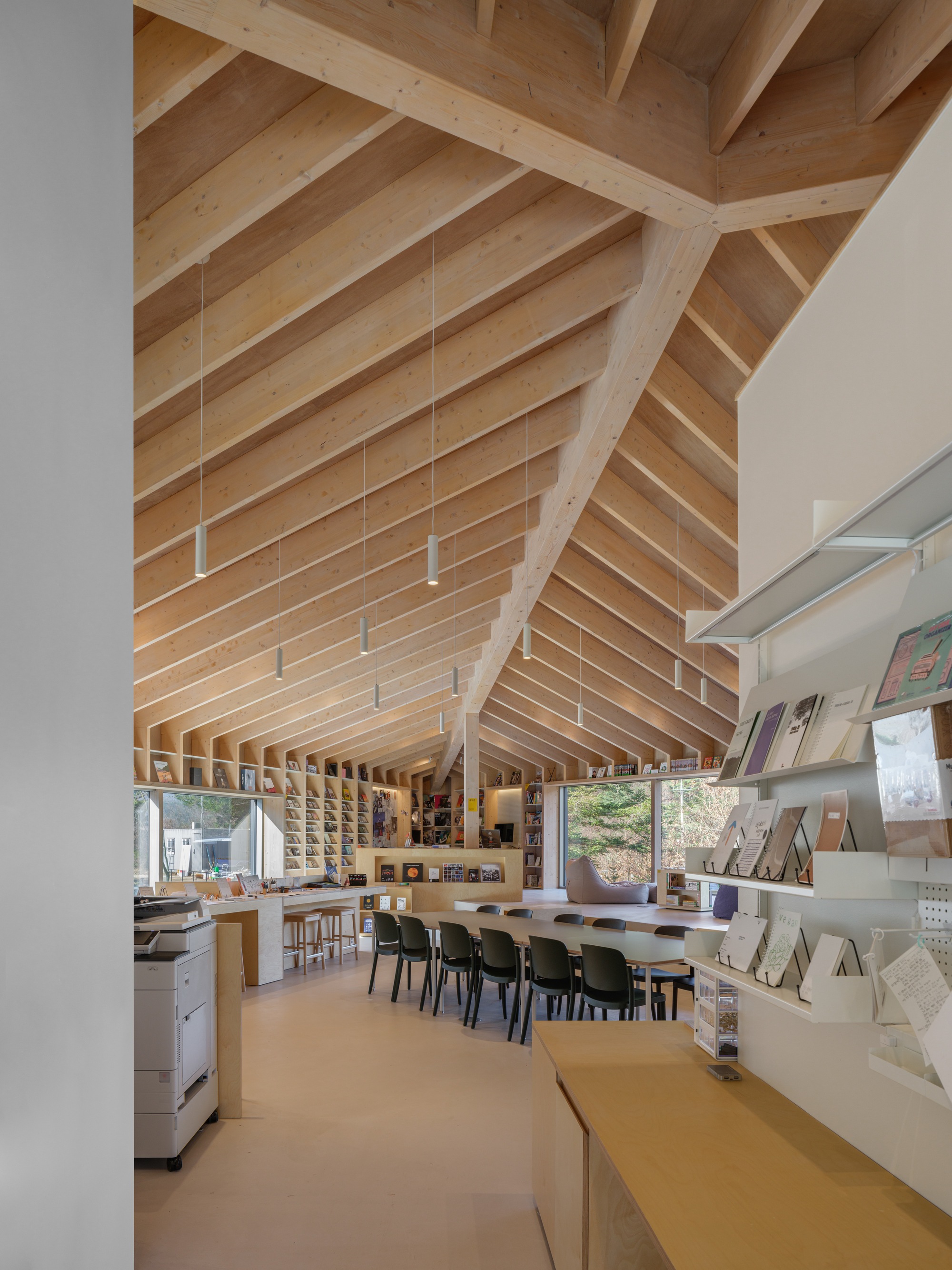 Interior workspace with exposed timber roof rafters and bookshelves below suspended pendant lights