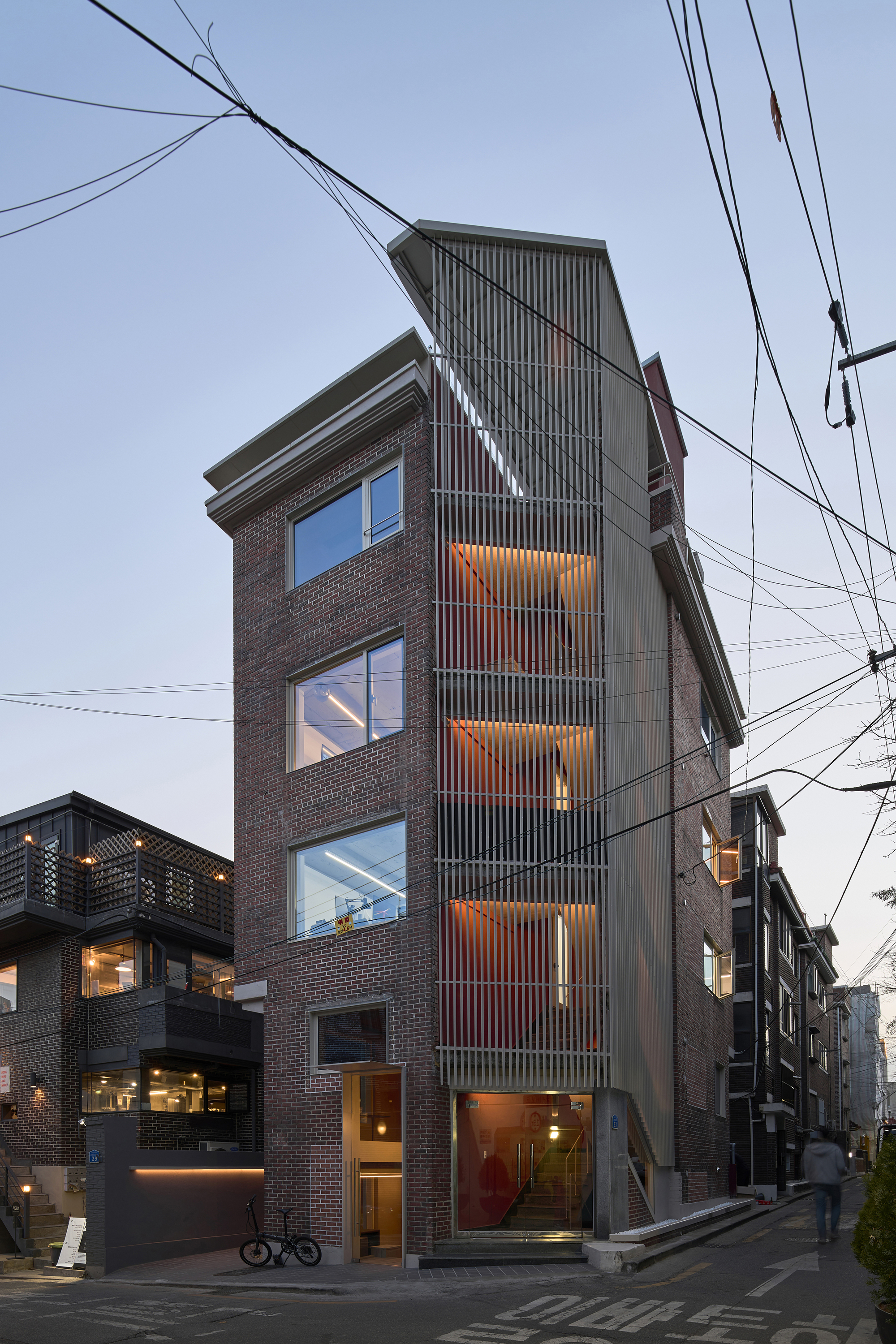 Street elevation of the vertical tower showing stacked windows and vertical metal screen at twilight