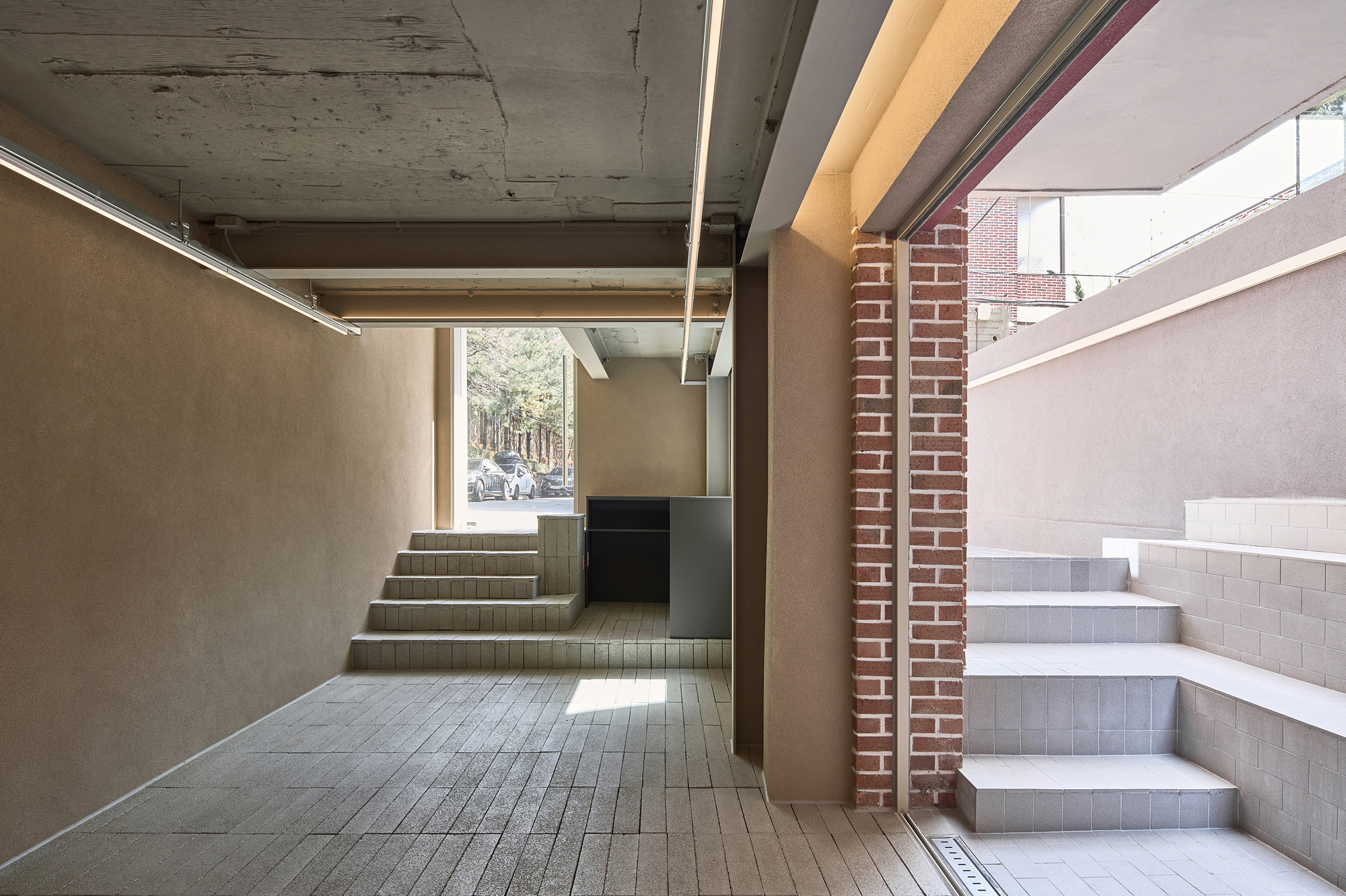 Interior entry hall with exposed concrete ceiling beams and two tiled staircases flanking a brick column