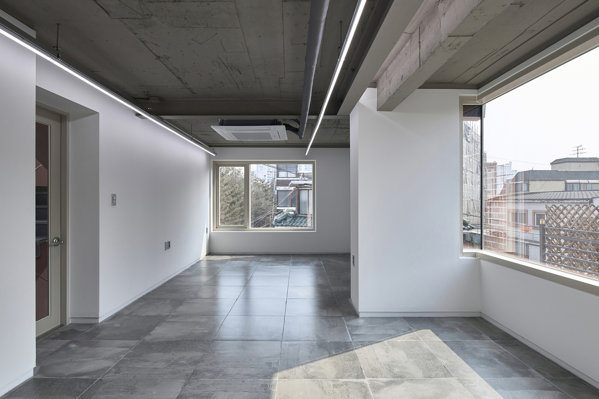 Open room with exposed concrete ceiling, linear lighting, and large-format grey floor tiles
