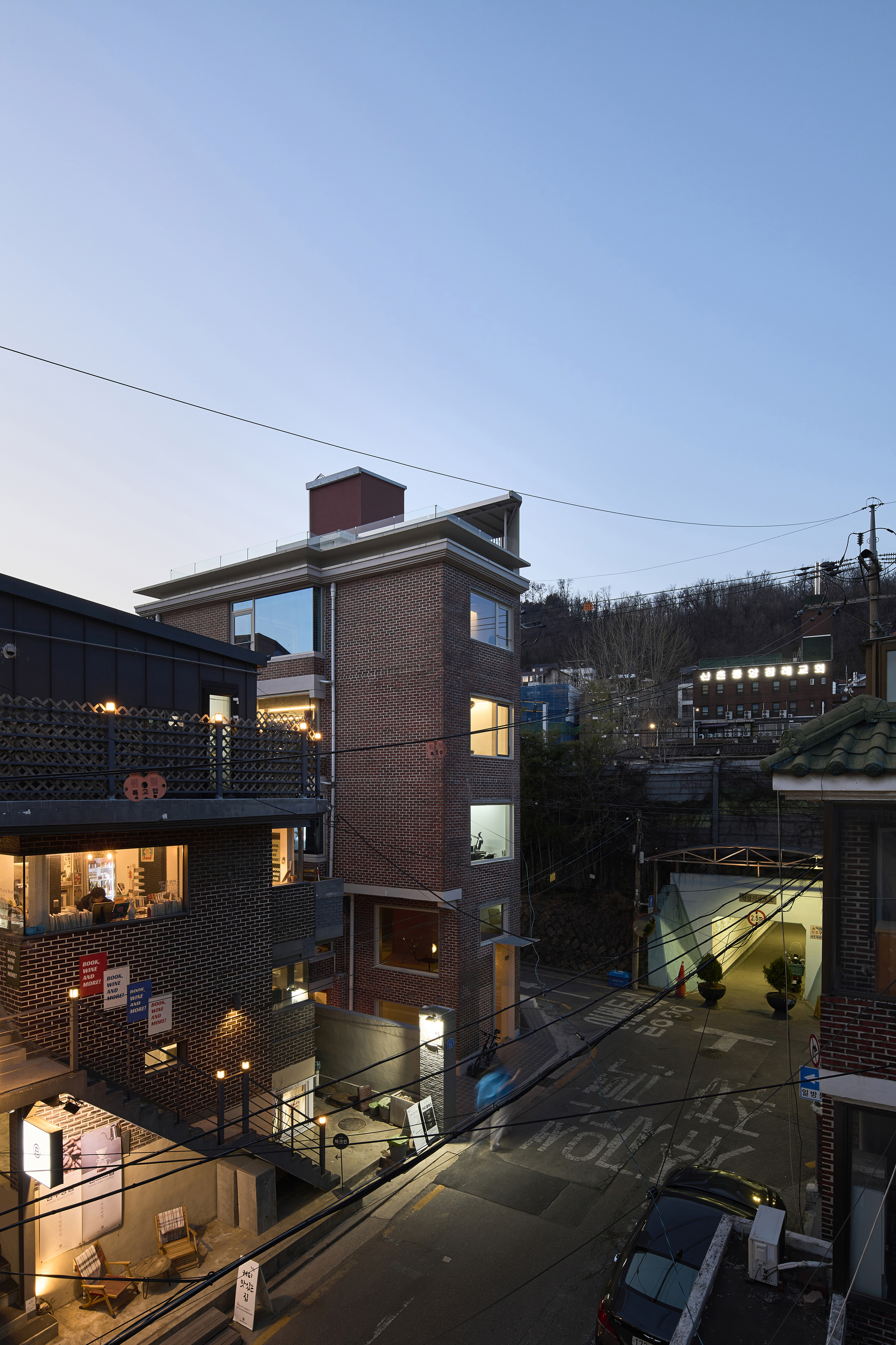Slender brick facade overlooking adjacent courtyards and rooftops illuminated in the blue hour