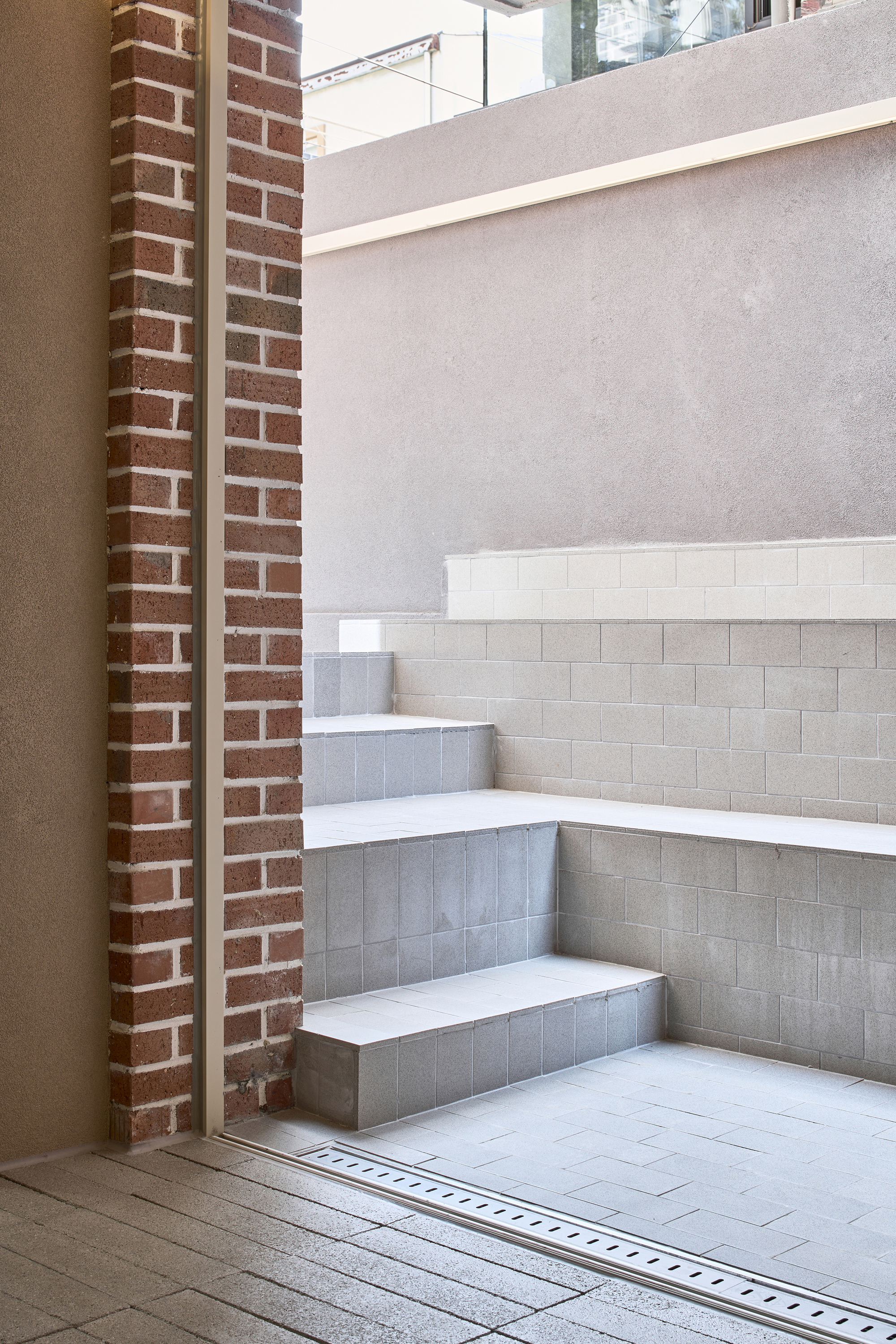 Corner stair with brick pilasters and white tile treads leading down to a linear drain