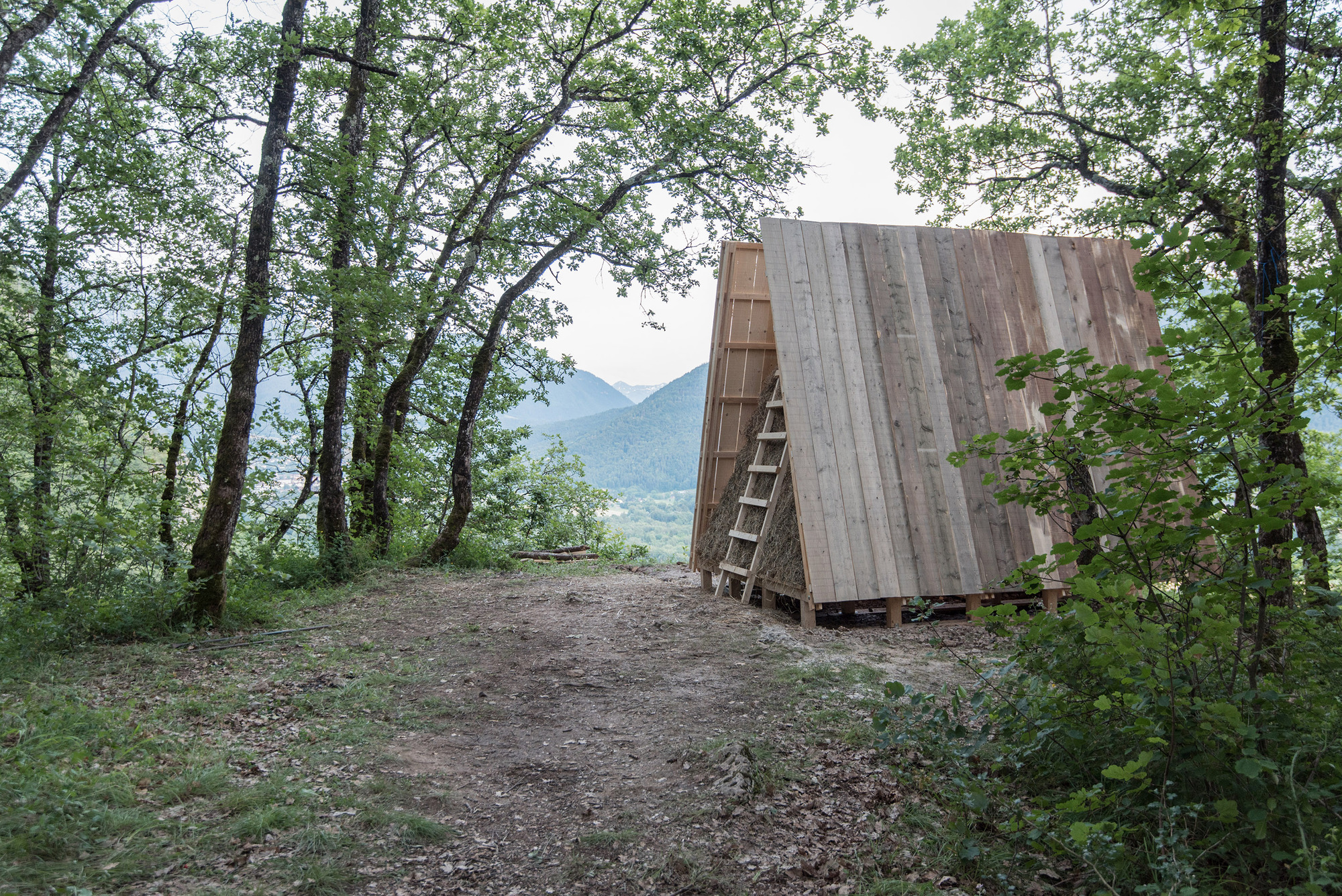 Weathered timber A-frame structure with ladder on a hillside overlooking distant mountains at dusk
