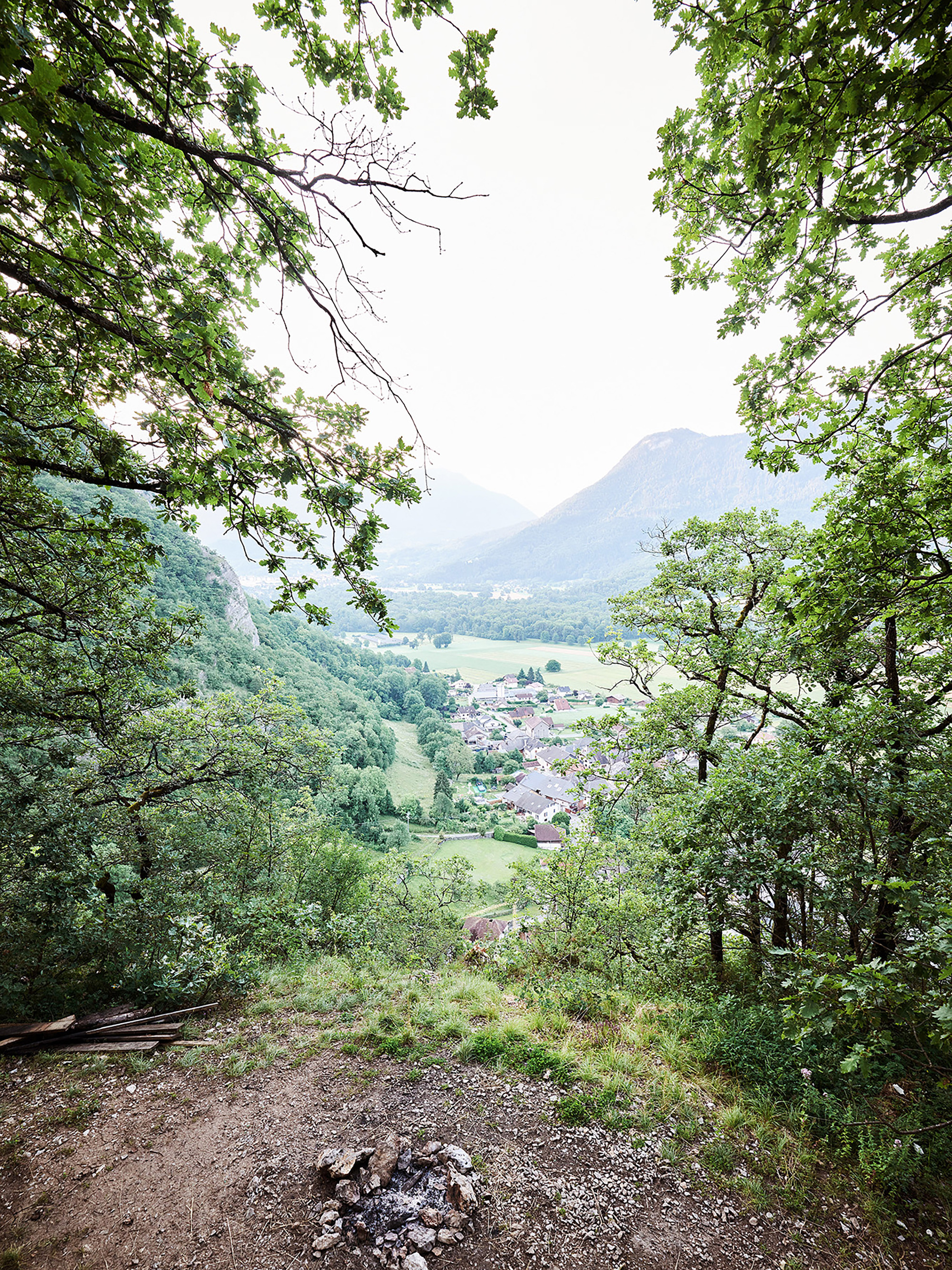 Valley view framed by tree branches overlooking a village and mountain in overcast light