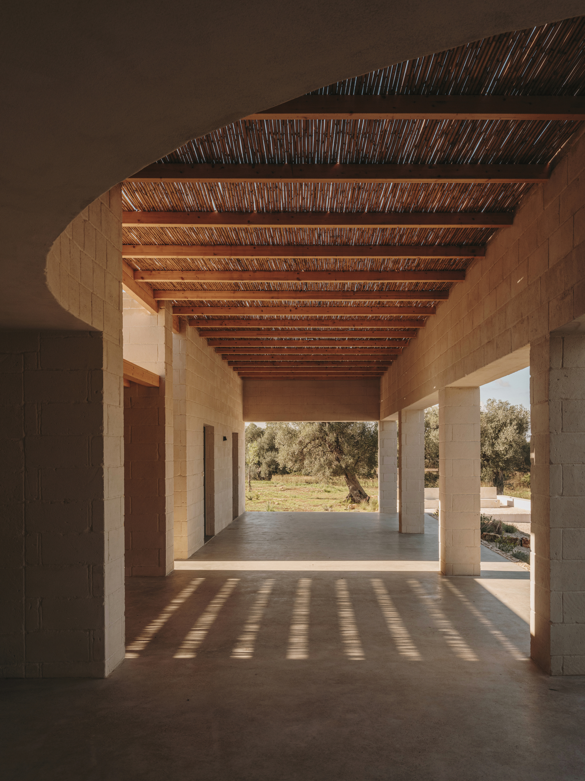 Covered corridor with timber beams and reed ceiling casting striped shadows on concrete floor