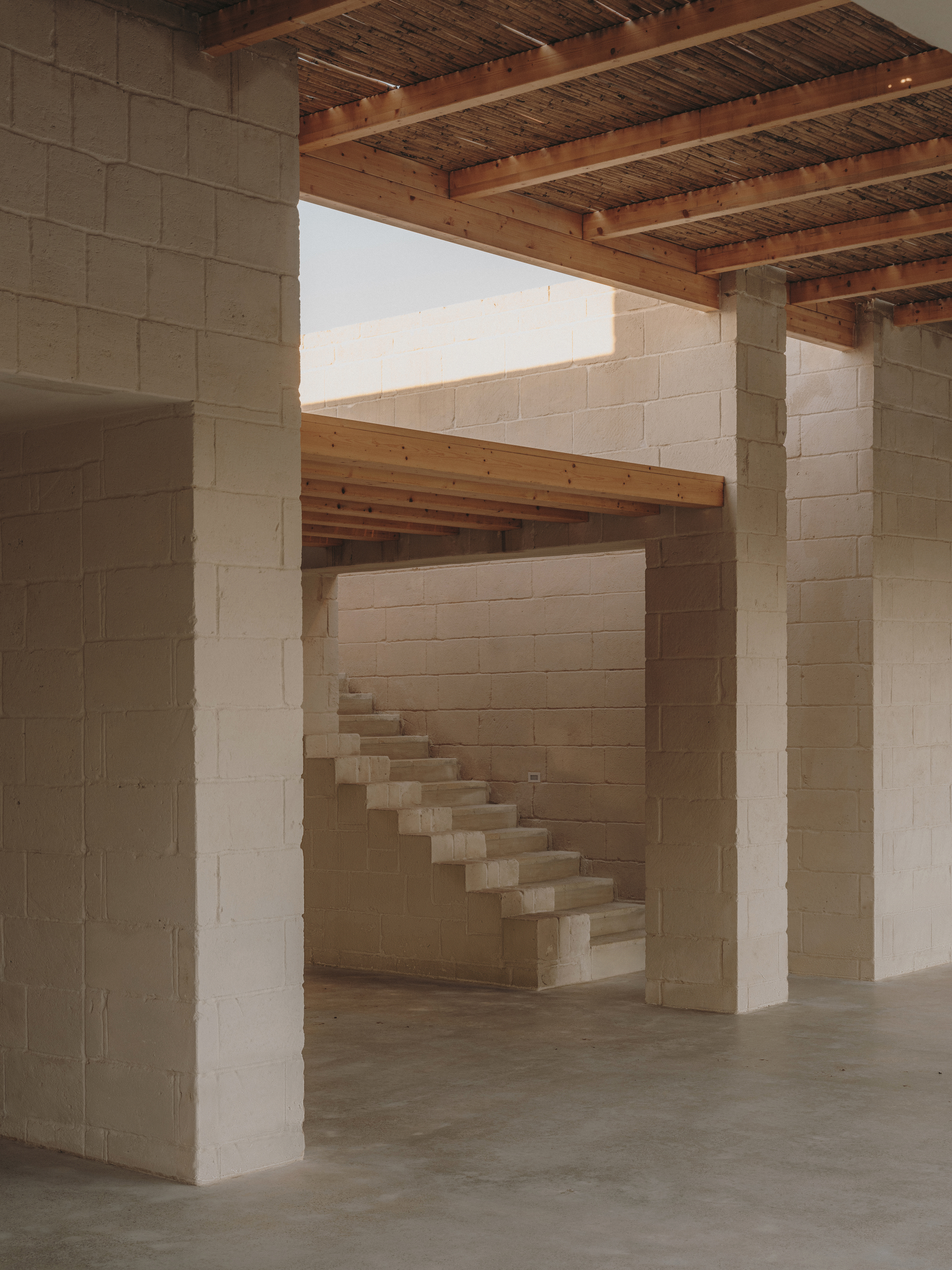 Interior view of cantilevered stone staircase through masonry columns under exposed timber joists