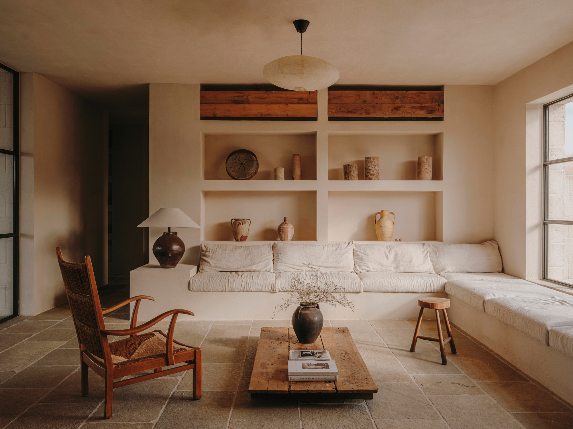 Living room with built-in shelving displaying terracotta vessels above a low upholstered banquette