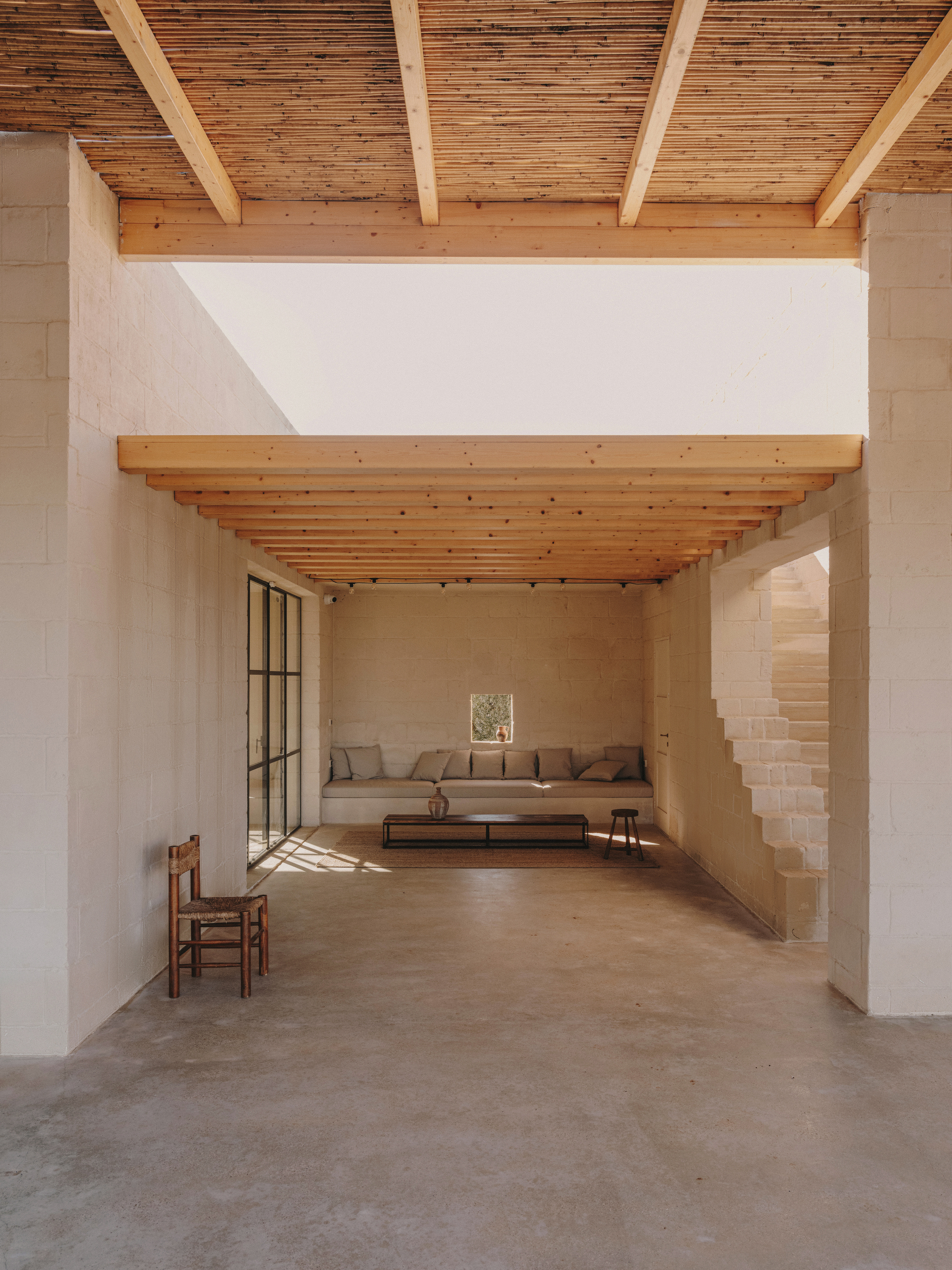 Interior space with exposed timber joists and beams connecting two seating areas in warm light