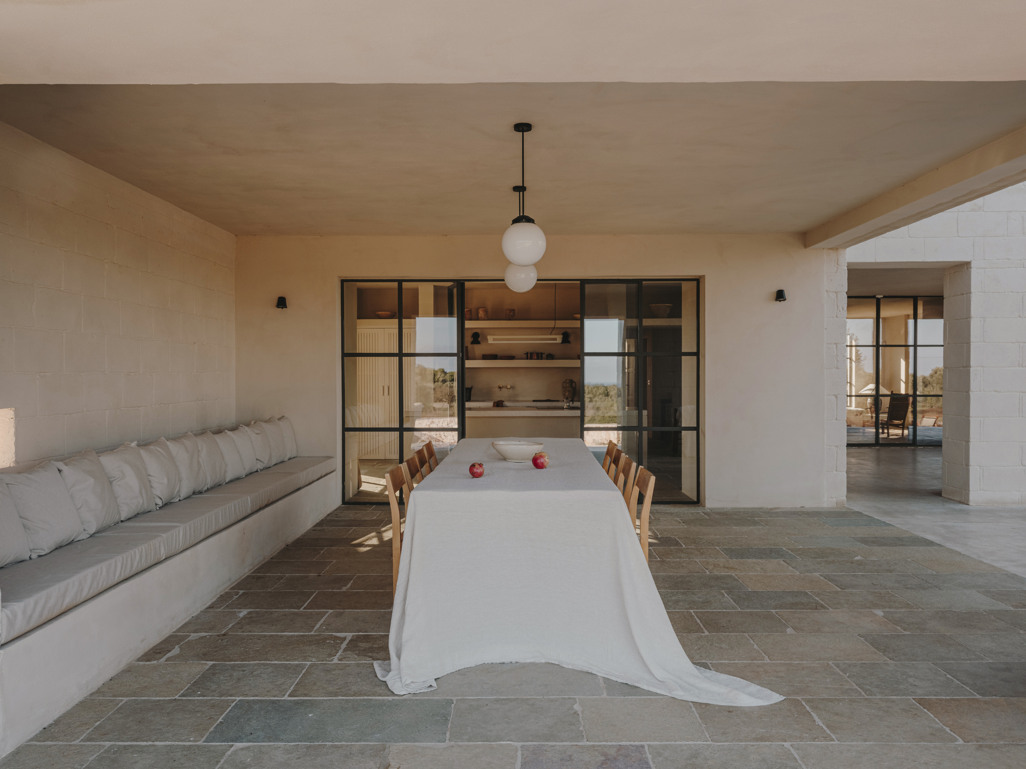 Open-plan dining room with steel-framed glass doors leading to the kitchen and stone tile floor