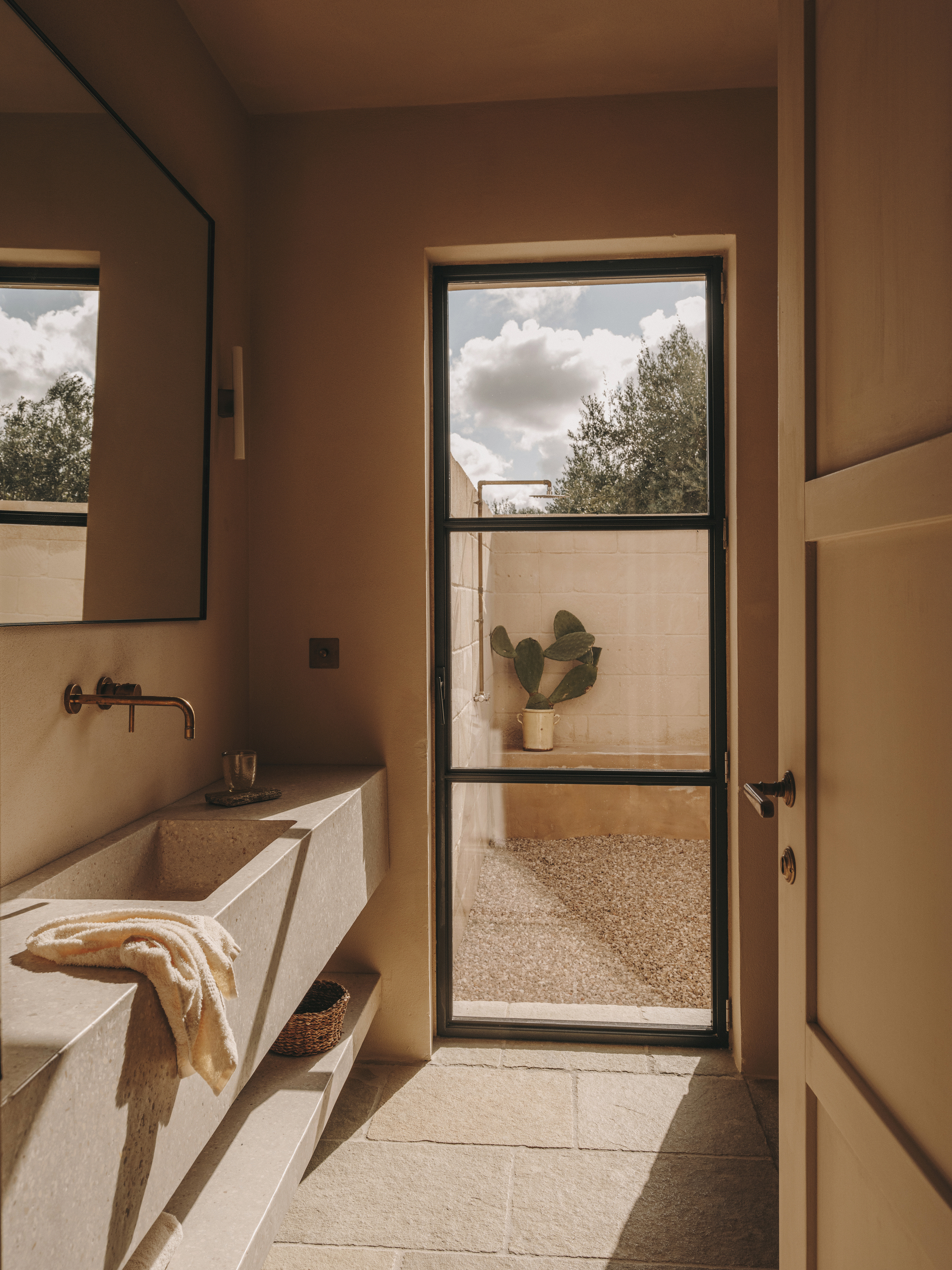 Bathroom with travertine vanity and black-framed door to an enclosed patio under billowing clouds