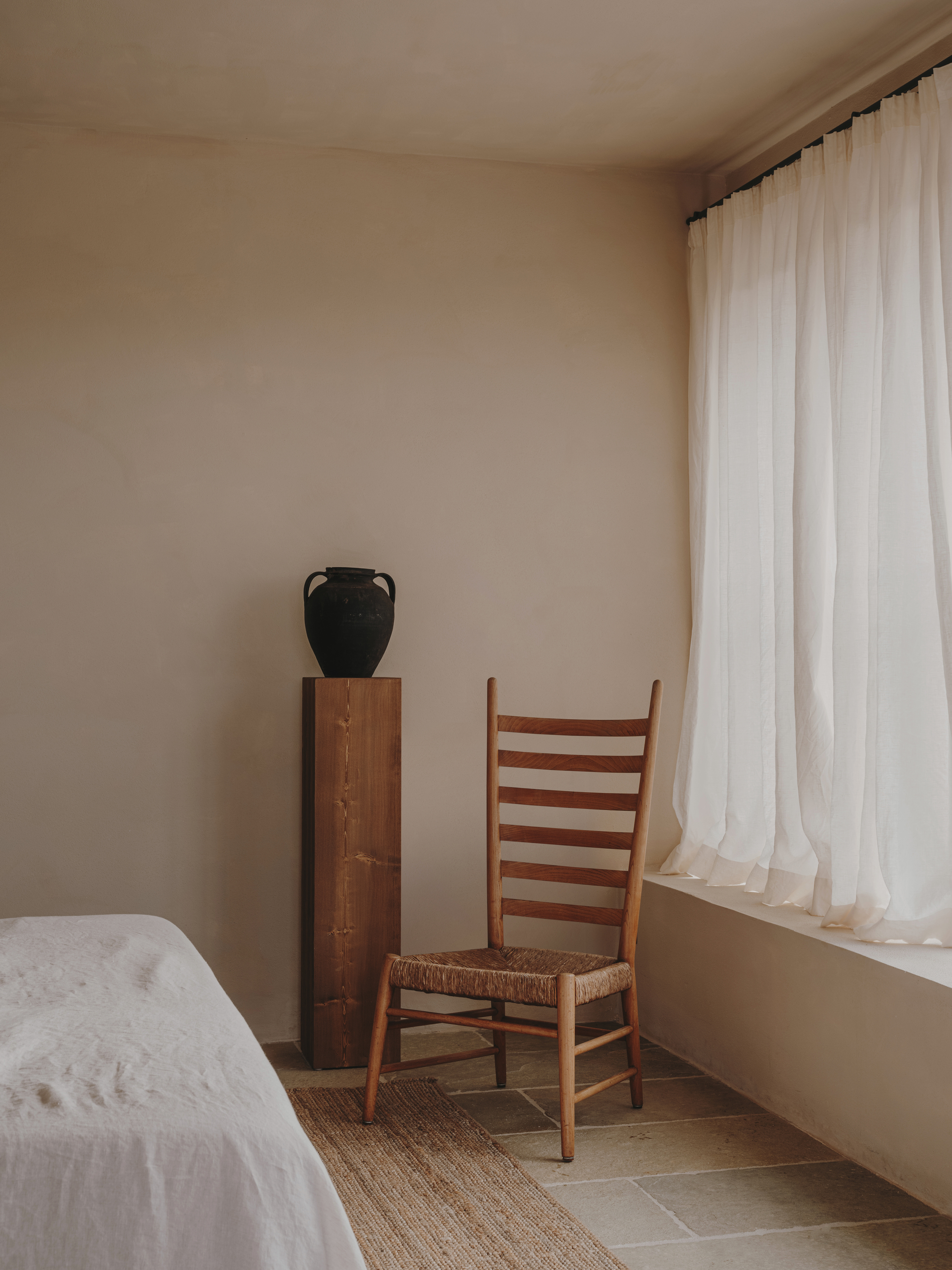 Bedroom corner detail showing a woven-seat chair and black vessel on an inlaid timber cabinet