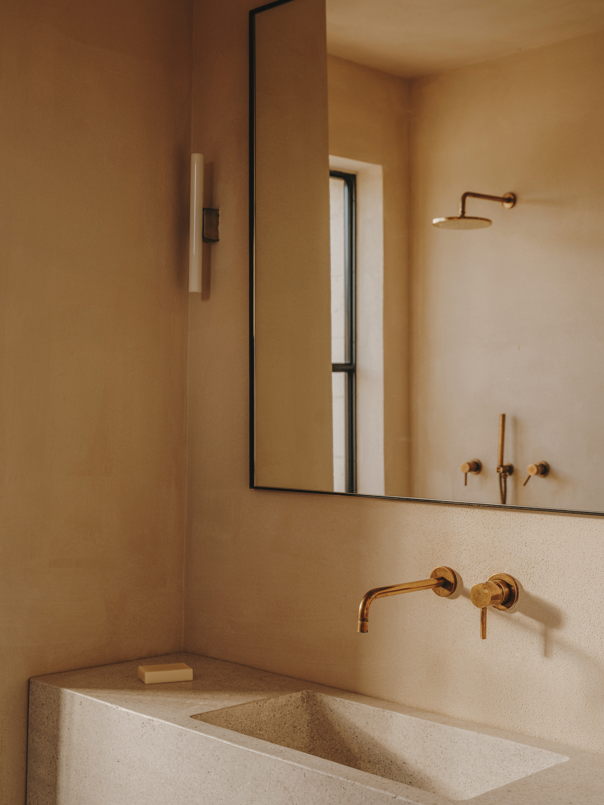 Bathroom vanity with integrated stone sink and brass wall-mounted faucet beneath a framed mirror