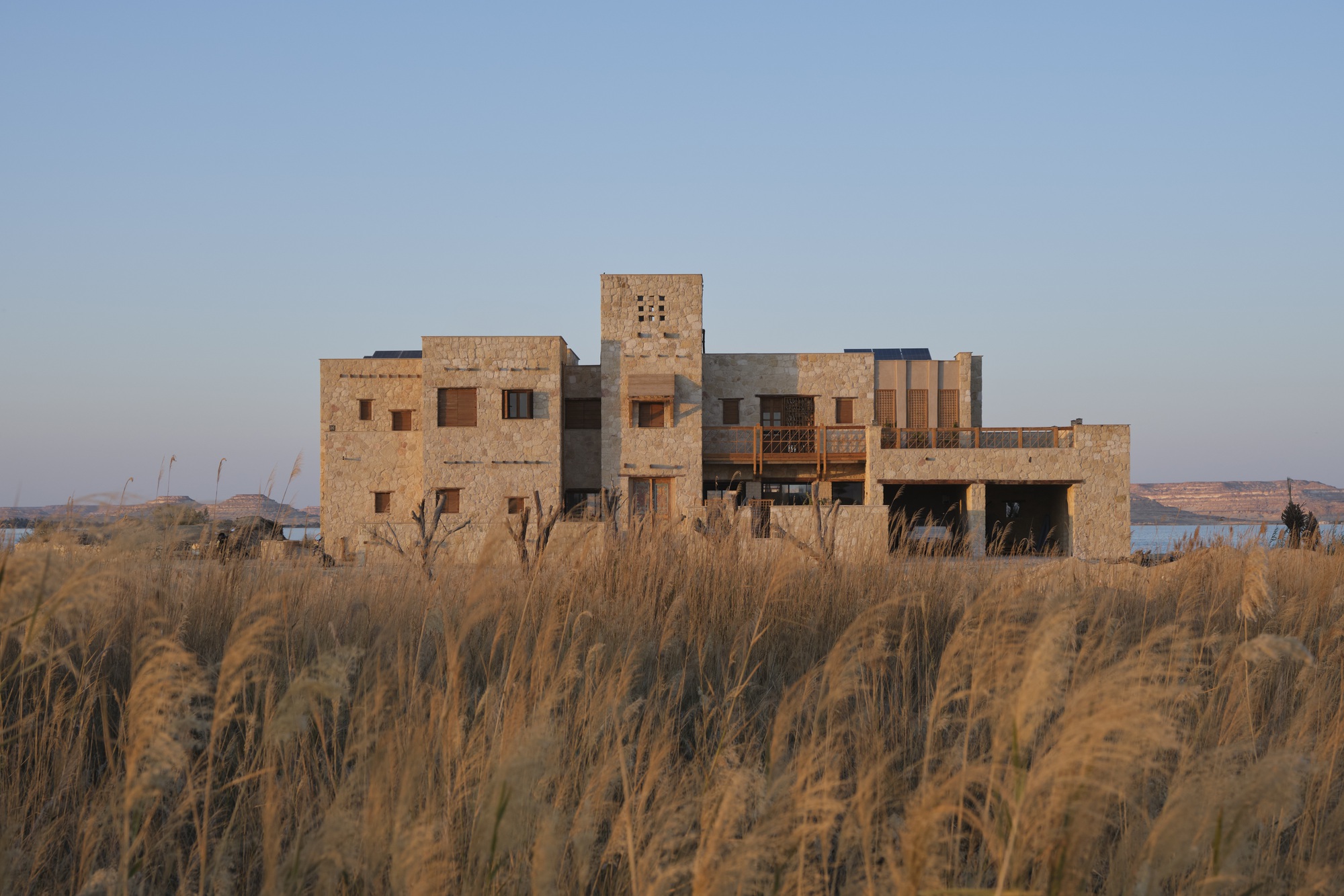 Rammed earth volumes with tower rising above golden grasses at dusk