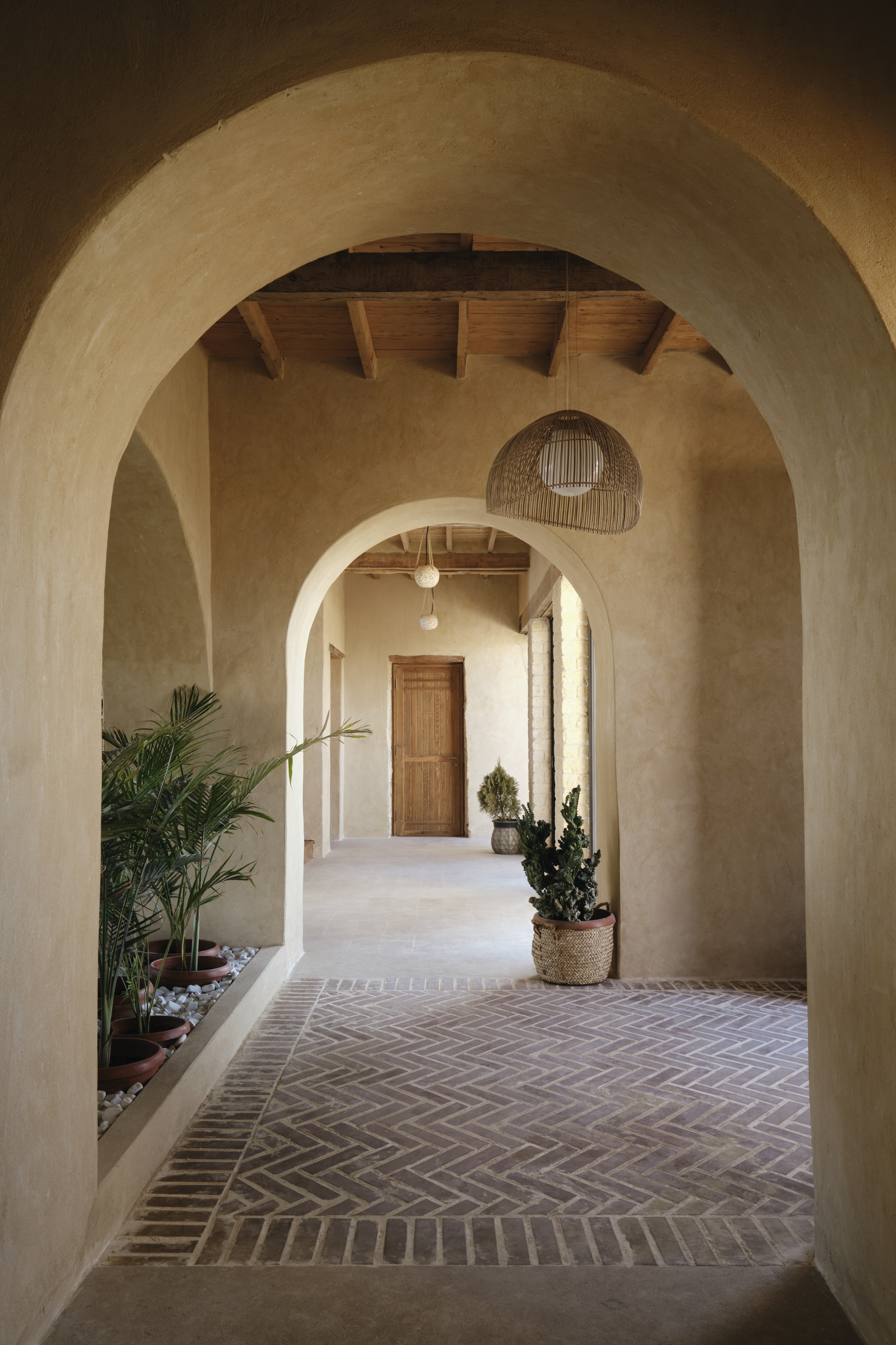 Sequence of plastered arches along a herringbone brick floor with potted plants