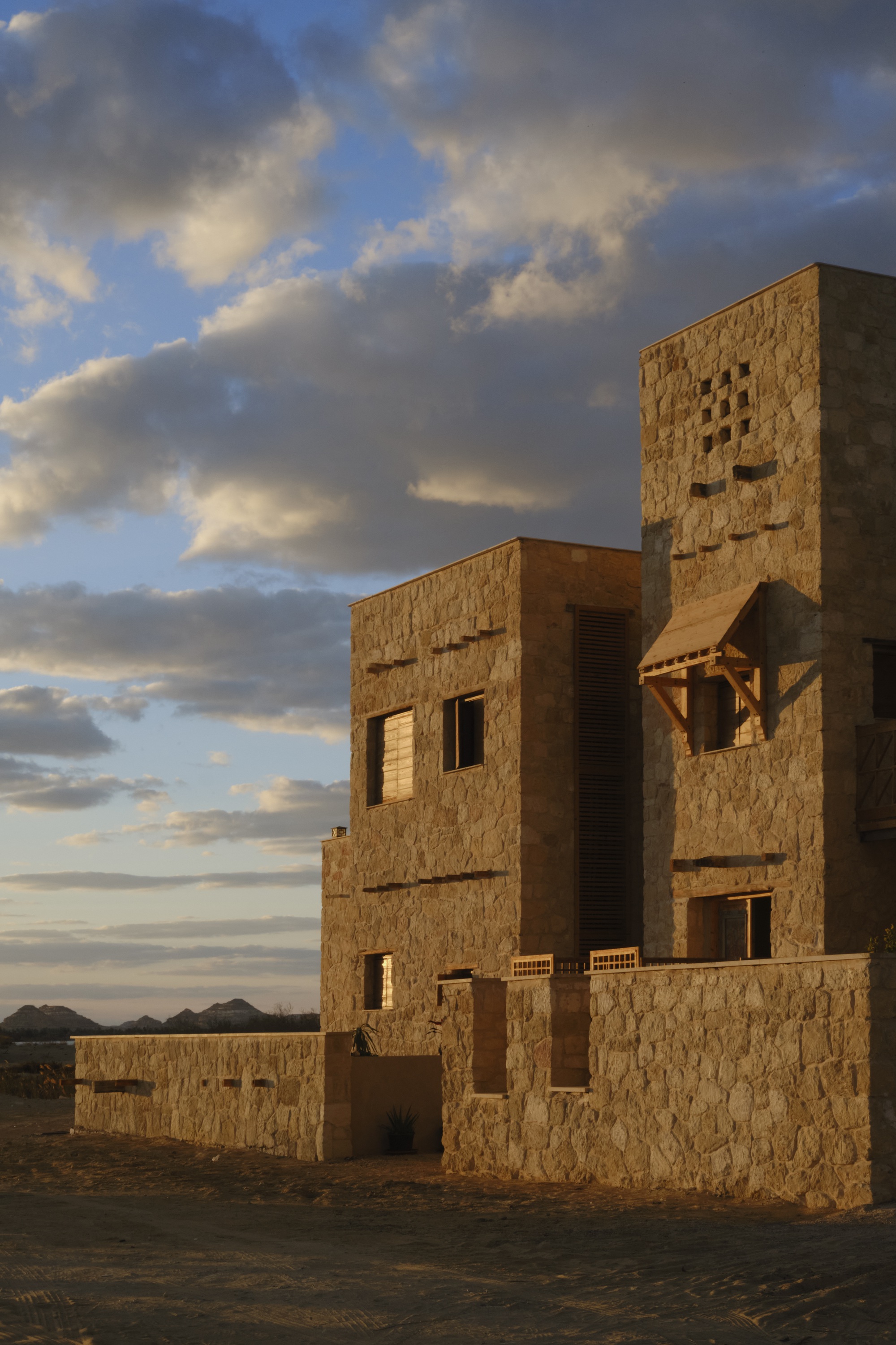 Stone block tower and connected volumes under a cloudy sky at sunset