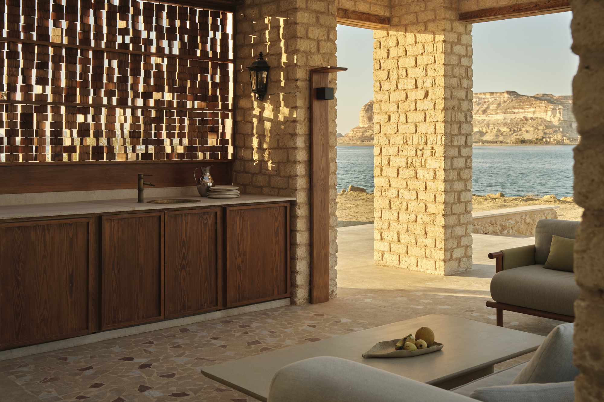 Open-air lounge with perforated brick screen wall and timber credenza overlooking calm water
