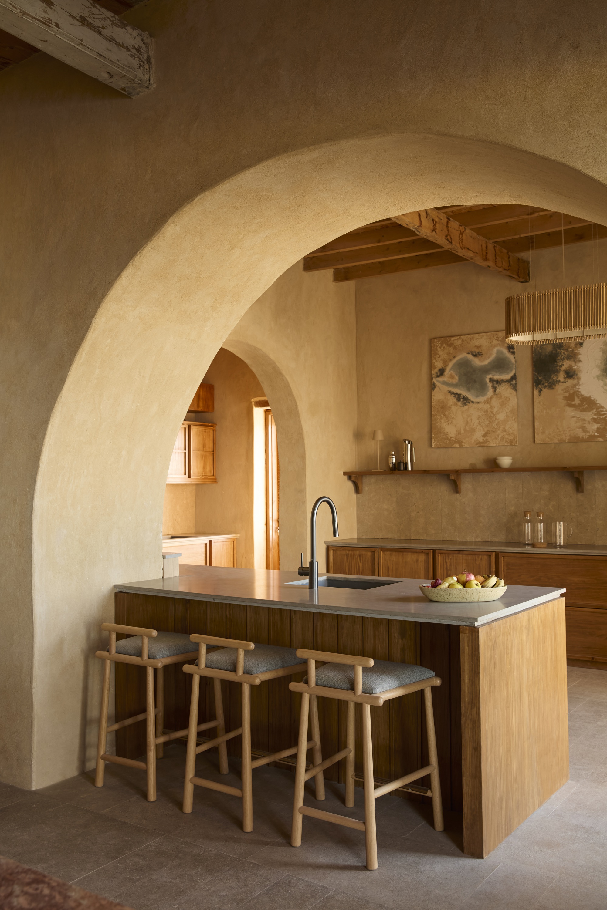 Kitchen island with three timber stools beneath a sequence of plastered arches