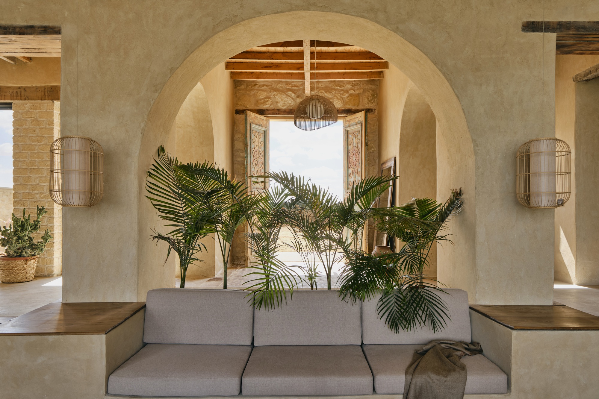 Layered arches framing a seating area with palm plants and woven wall sconces