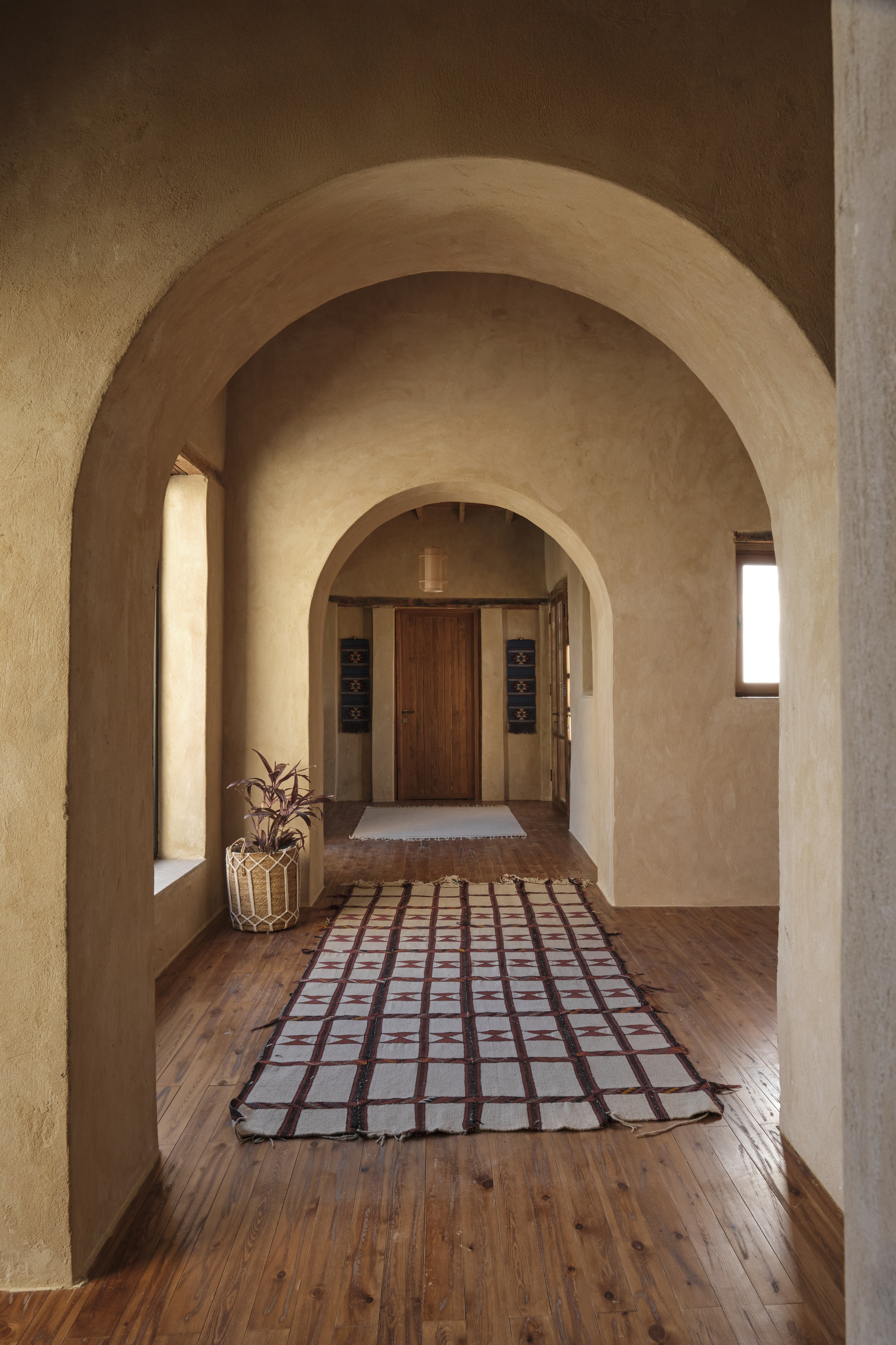 Corridor with nested barrel vaults and gridded runner rug leading to a timber door