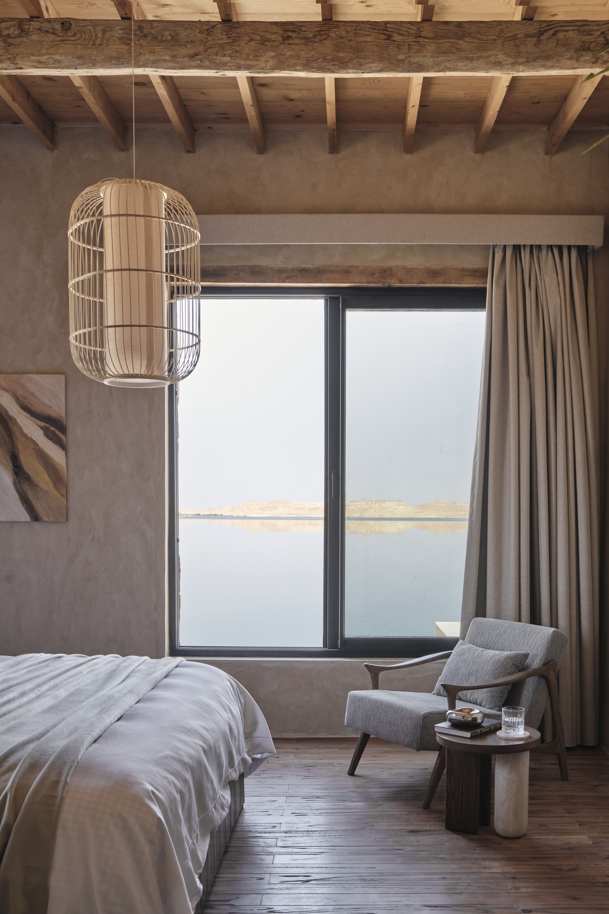 Bedroom interior with exposed timber ceiling joists and a cage pendant light beside the window