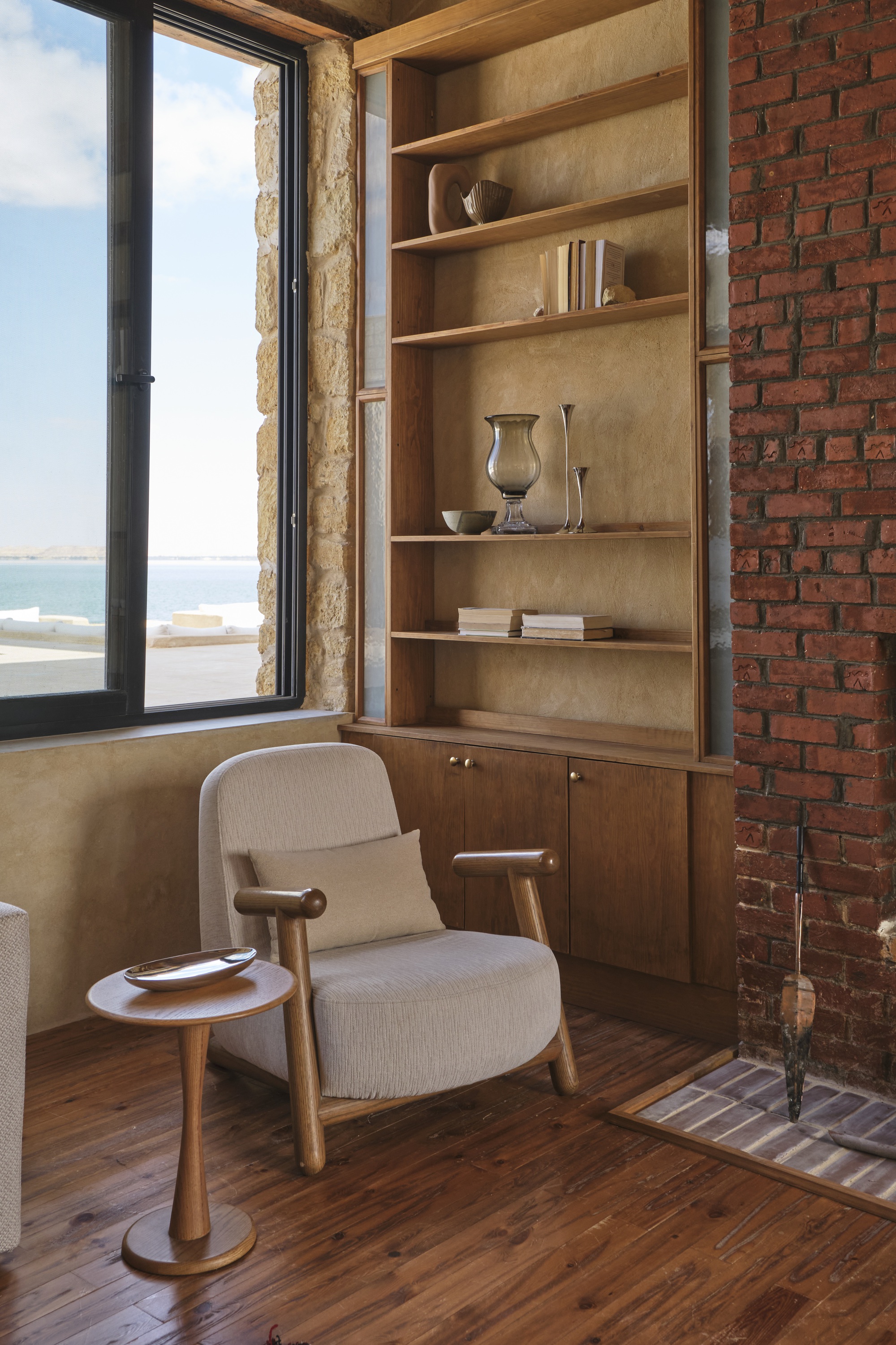 Built-in timber shelving unit next to exposed brick wall with an armchair near the open window