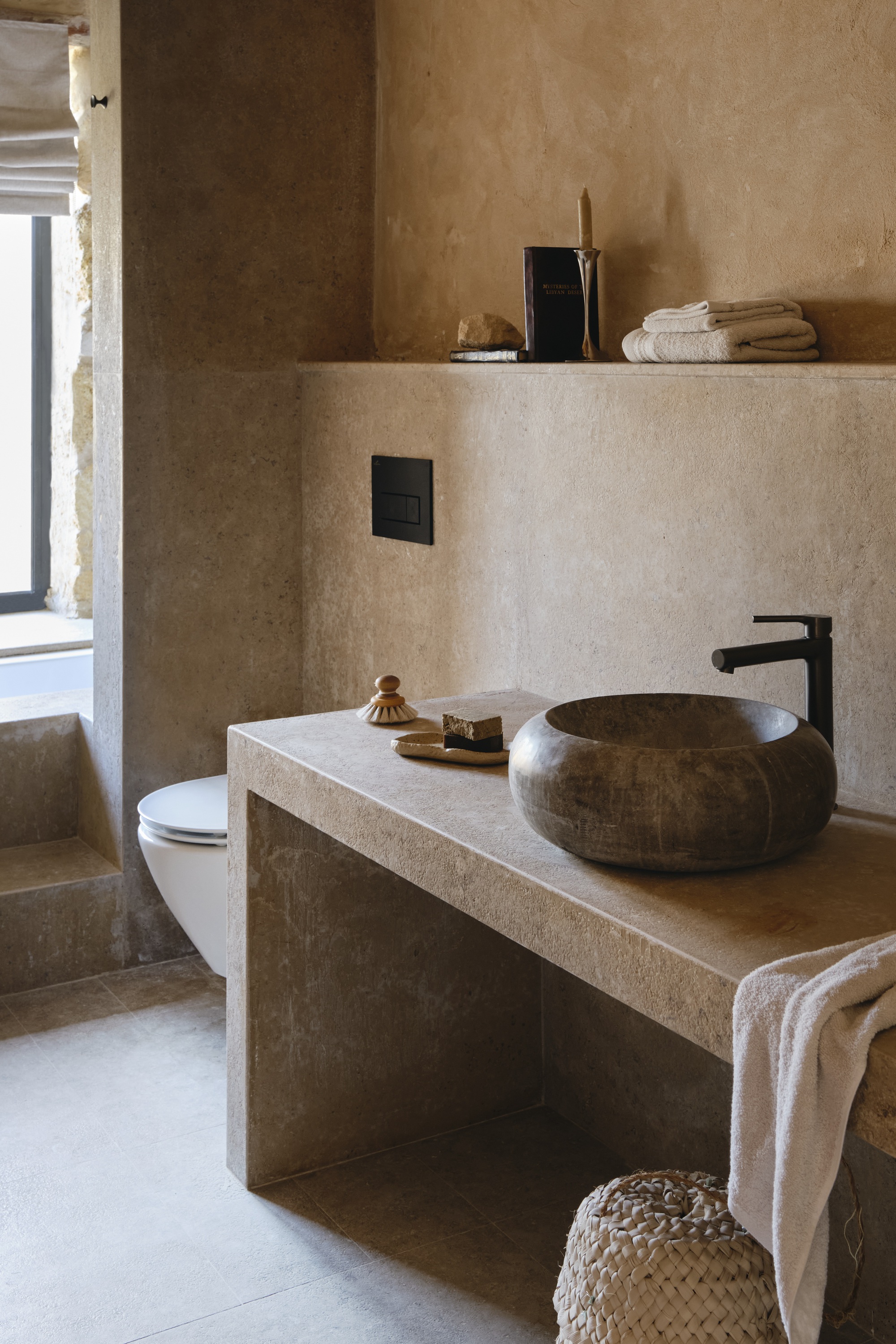 Bathroom vanity with rounded stone vessel sink and integrated floating shelf in textured plaster