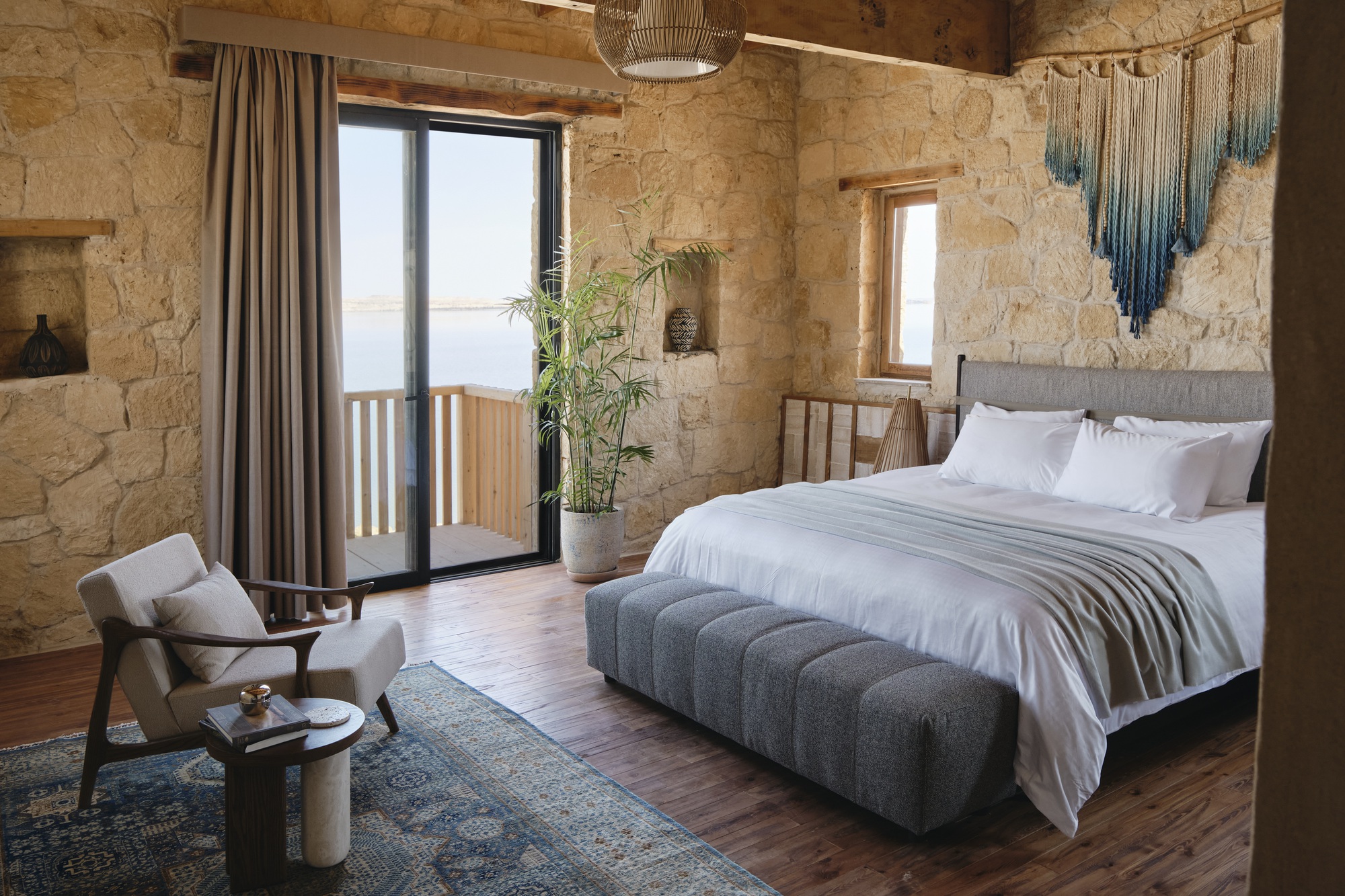 Bedroom with rough stone walls and timber balcony doors opening to daylight over the water