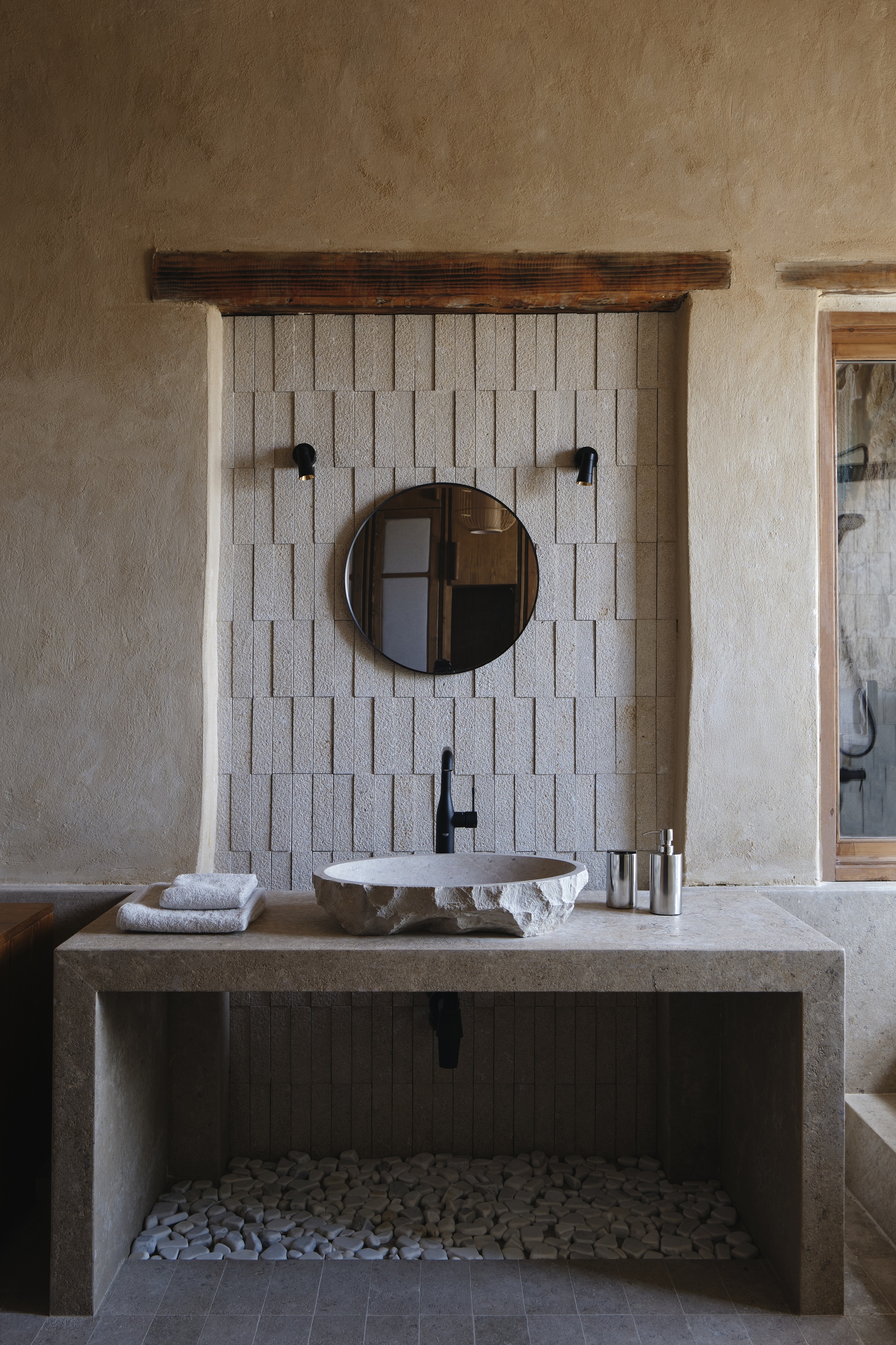 Concrete vanity console with white tile accent wall and circular mirror in textured plaster bathroom