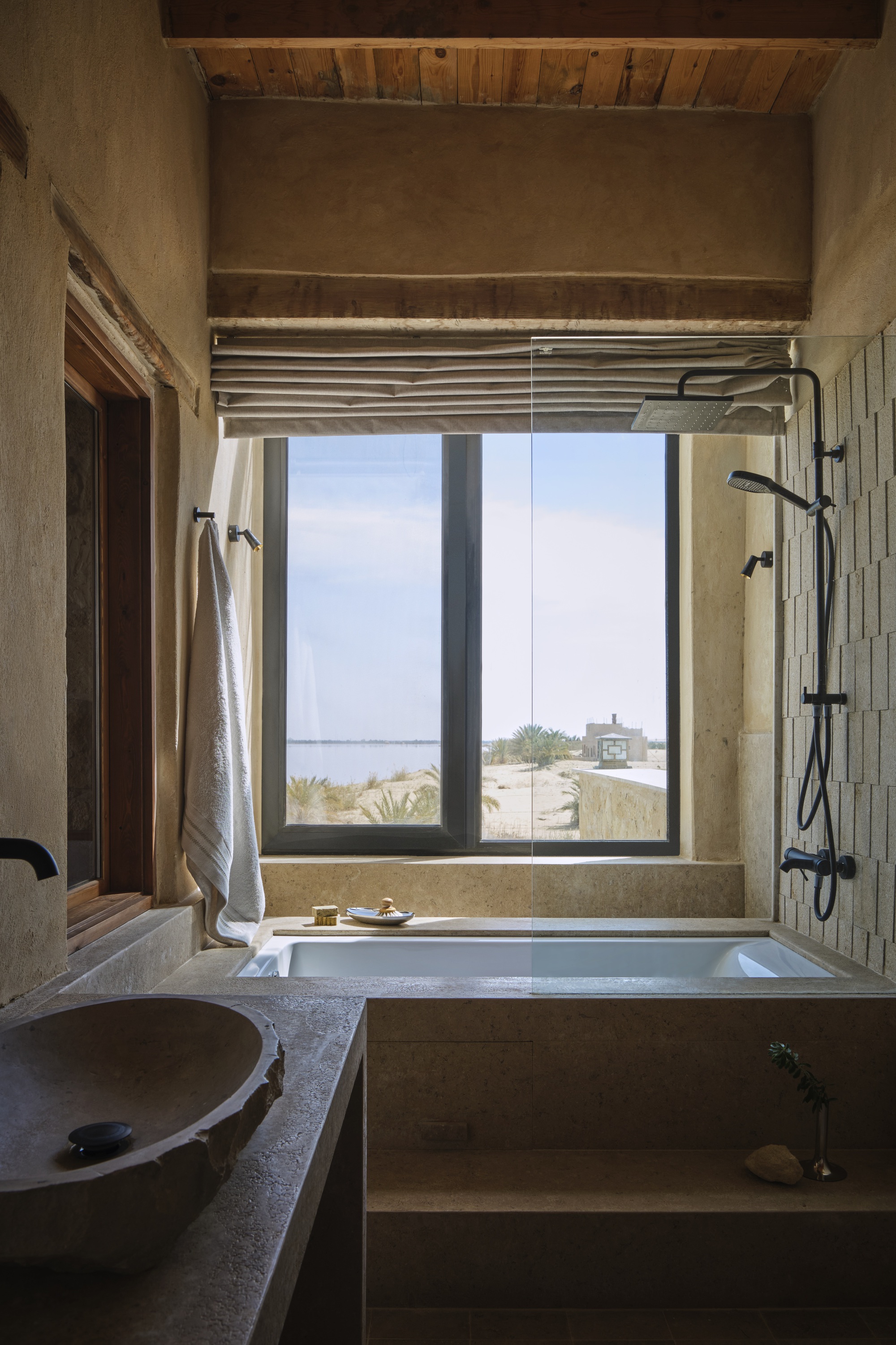 Bathroom with sunken tub and window framing coastal view with exposed timber ceiling above