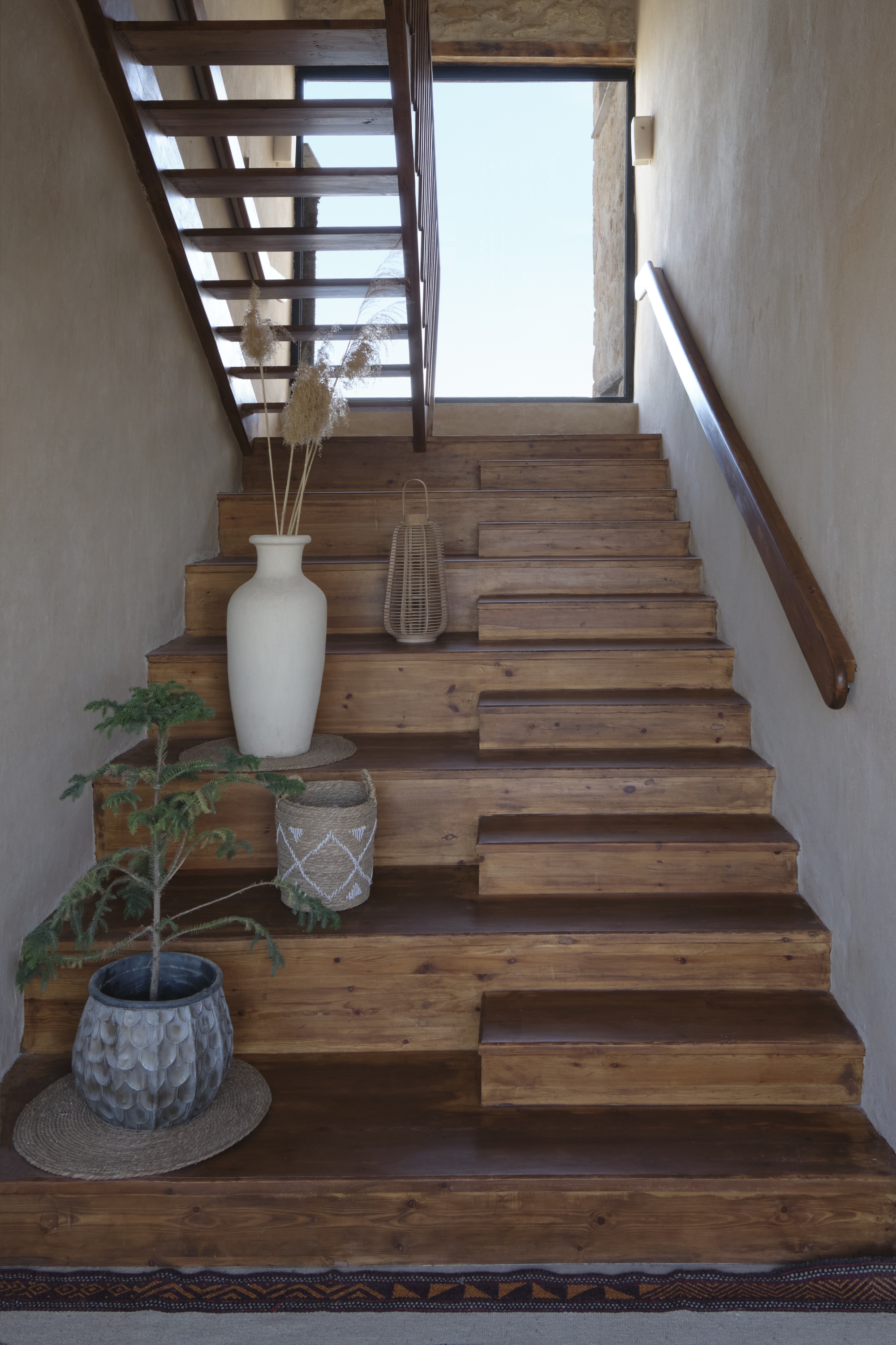 Timber staircase with open risers and planted vessels at base beside textured plaster walls