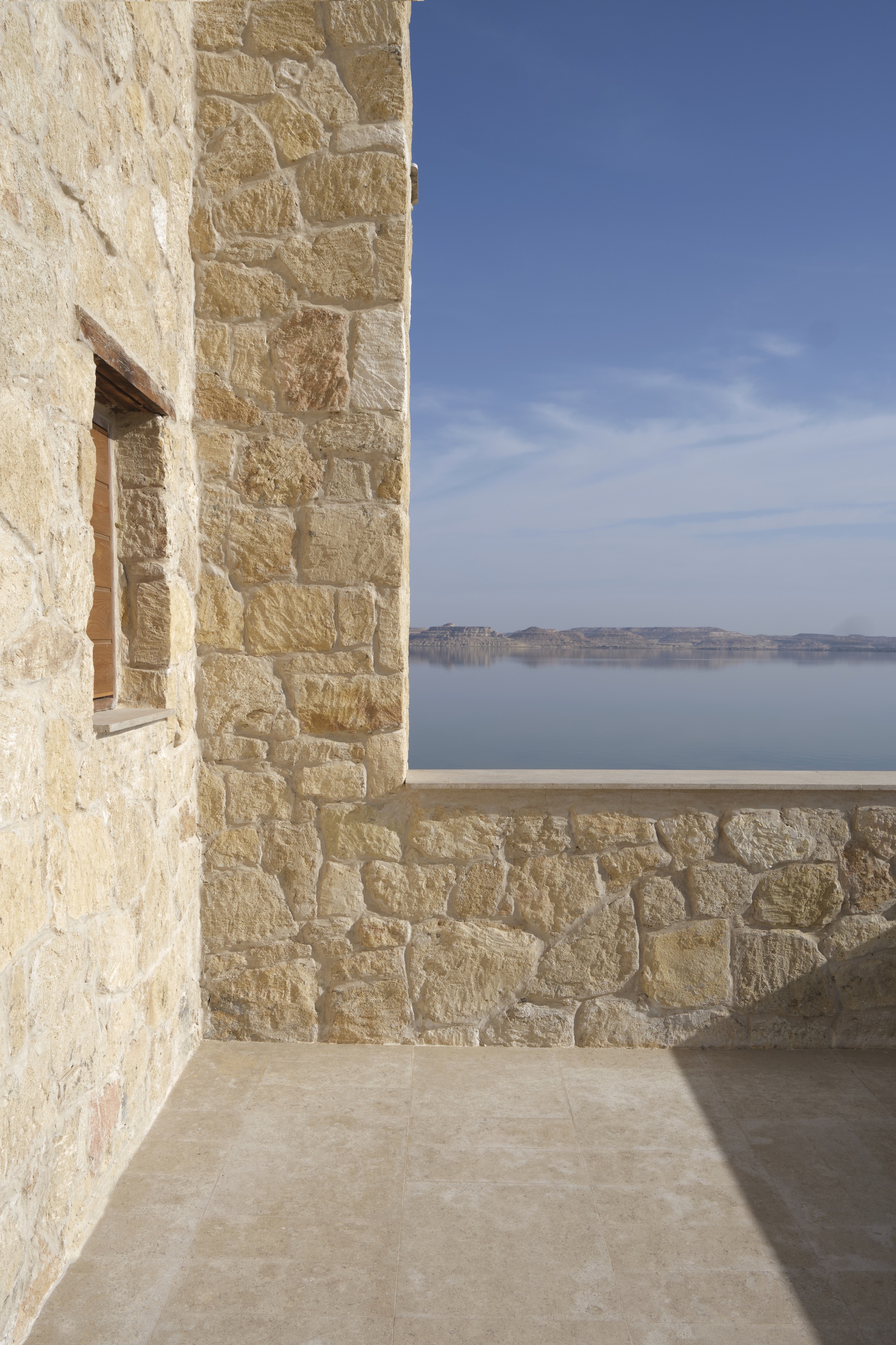 Corner terrace with limestone walls overlooking calm water under clear blue sky