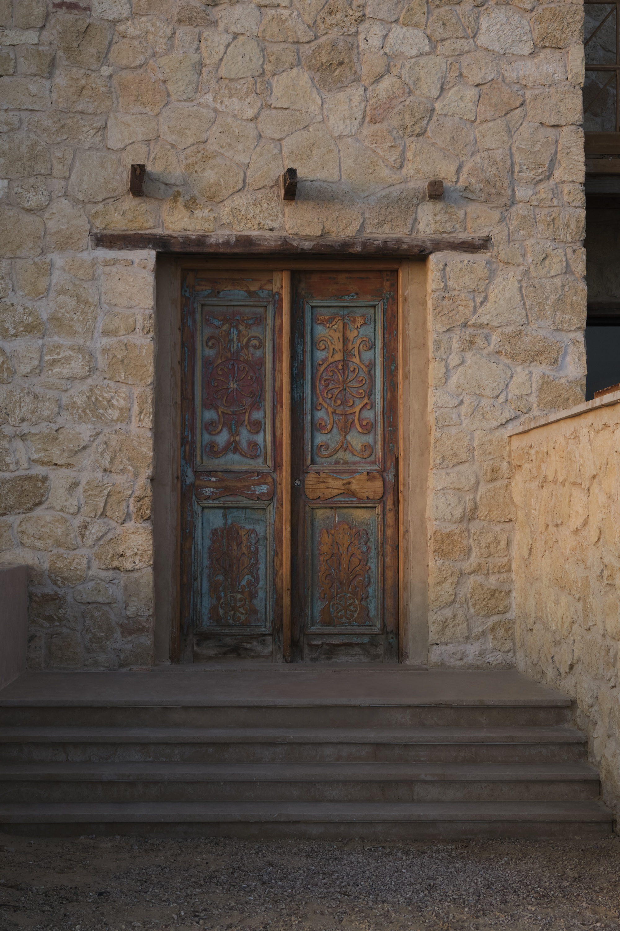 Weathered painted wooden double doors set into a coursed stone wall with timber lintel and iron brackets