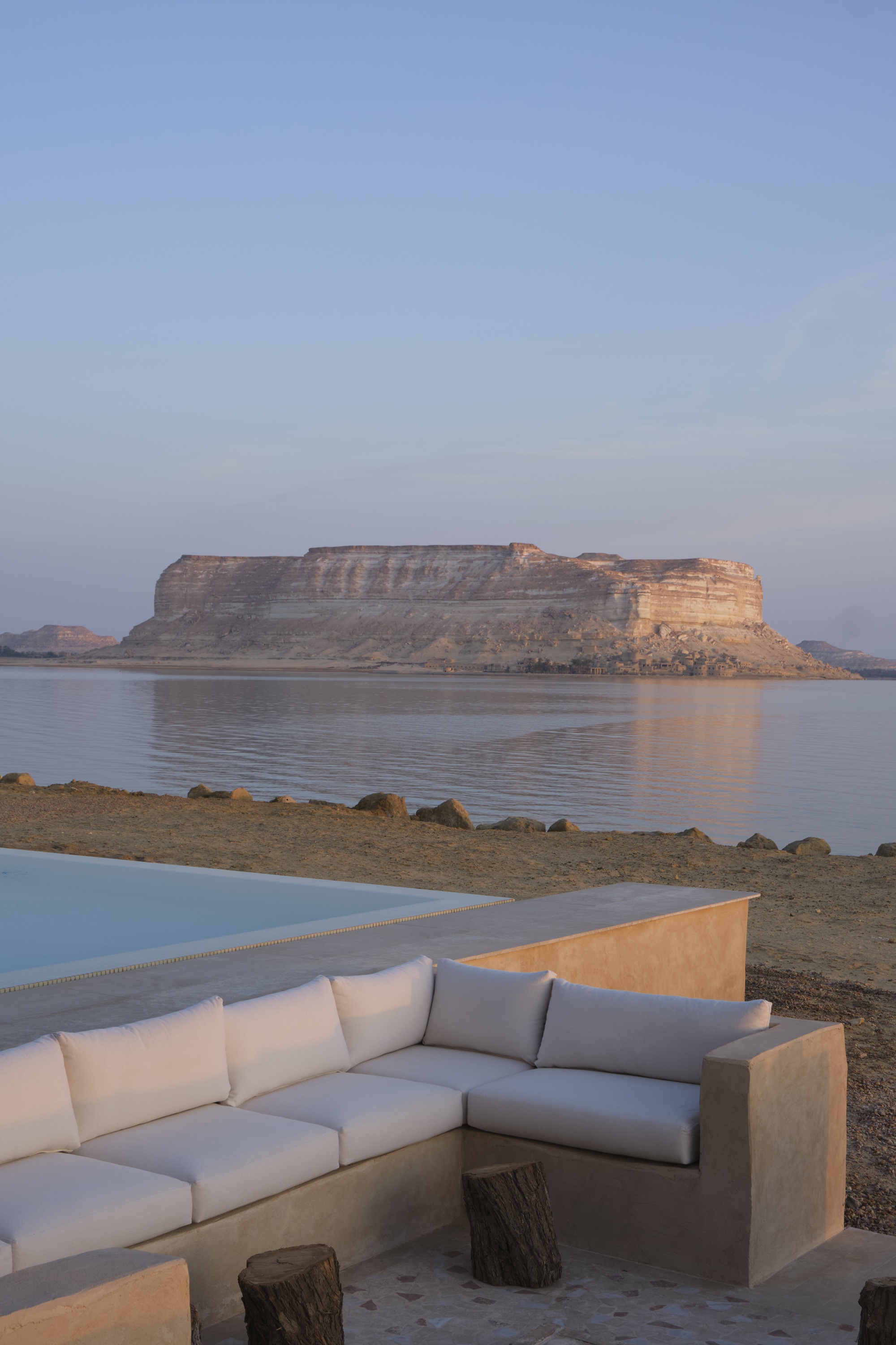 Sunken limestone seating area beside a pool with stratified rock formations reflected in still water at dusk