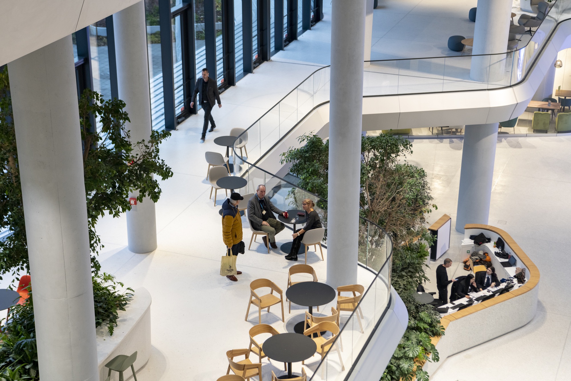 View down into the atrium showing curved balconies with seating areas, planters, and people gathered in conversation