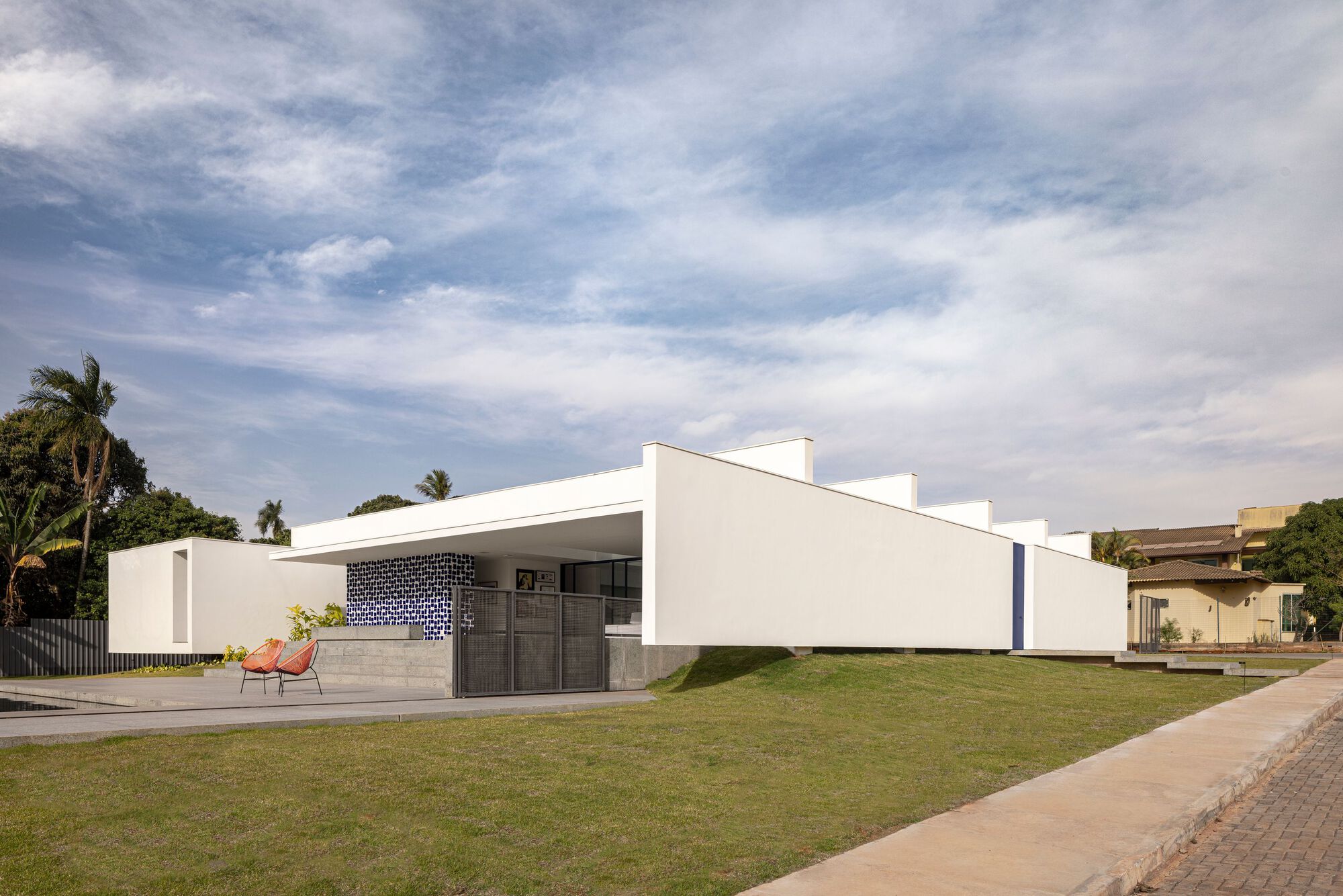 Street view of the white stucco facade with dark tiled portal and low concrete bench under palm trees