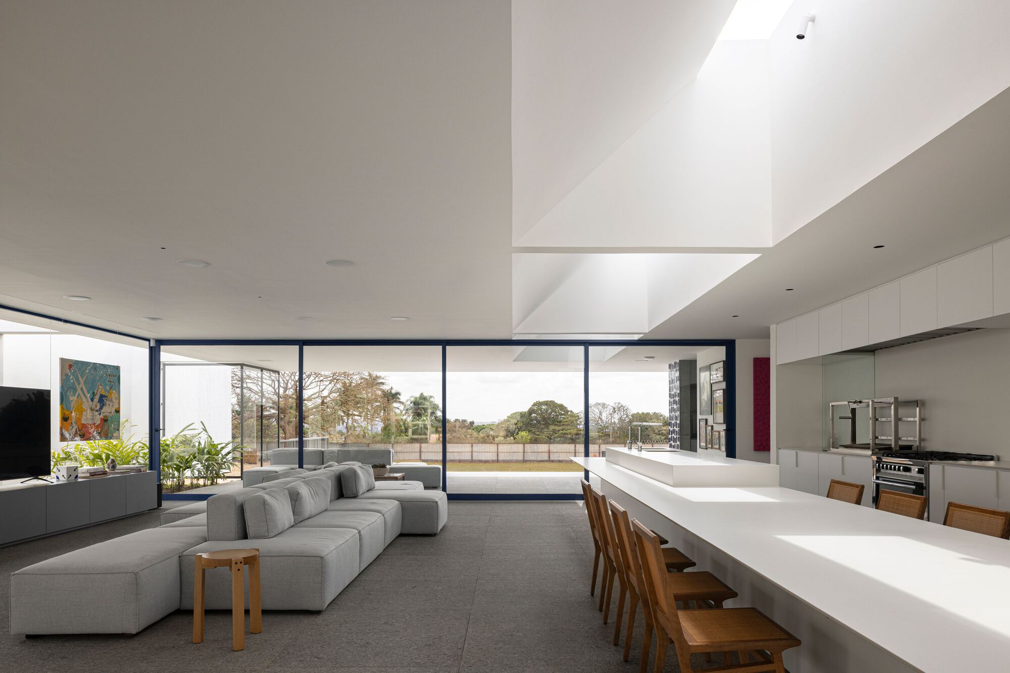 Open-plan living space with floor-to-ceiling glazing opening to lawn and double-height skylit void above