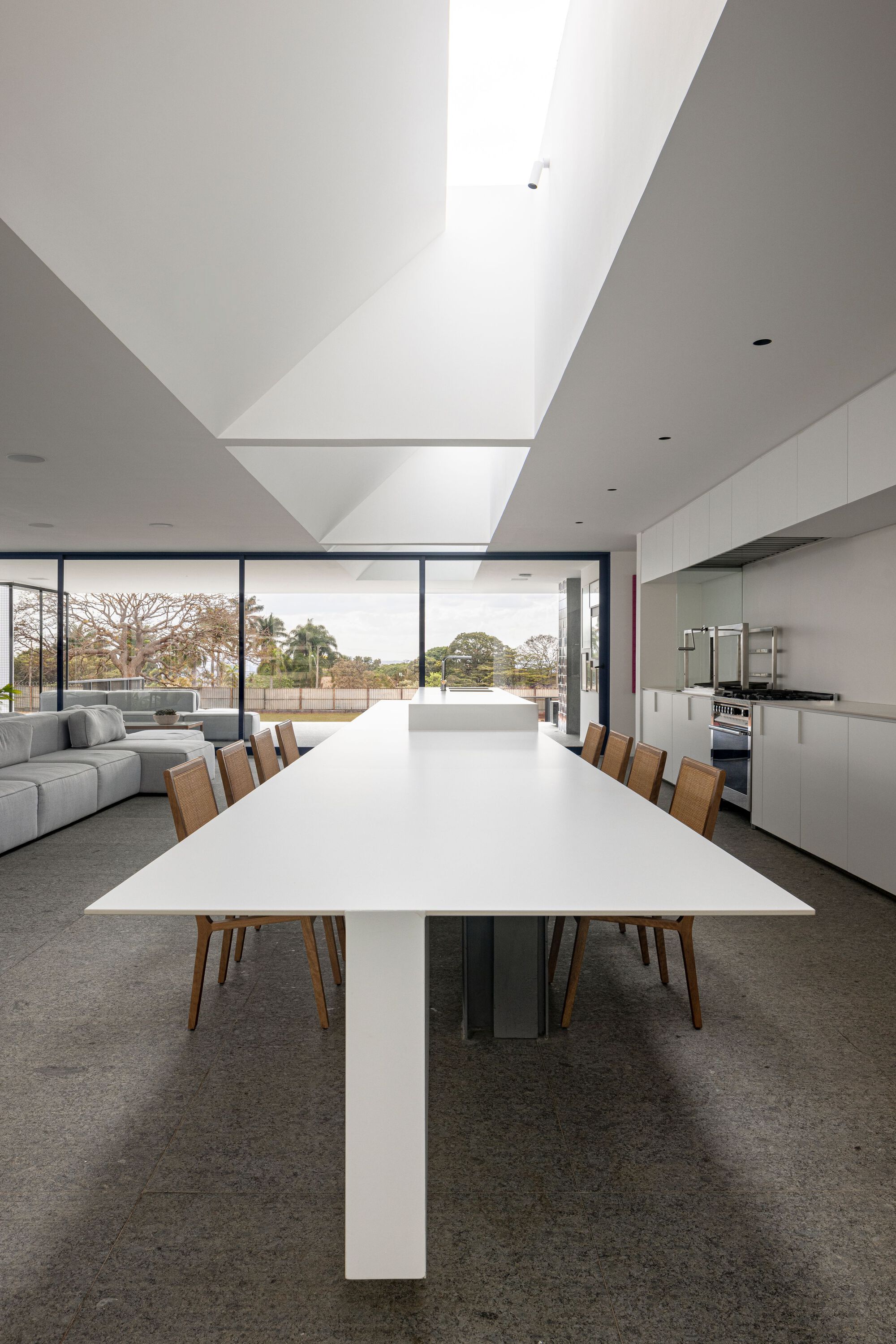 Open-plan living and dining space with long white table beneath angular folded ceiling plane and clerestory window