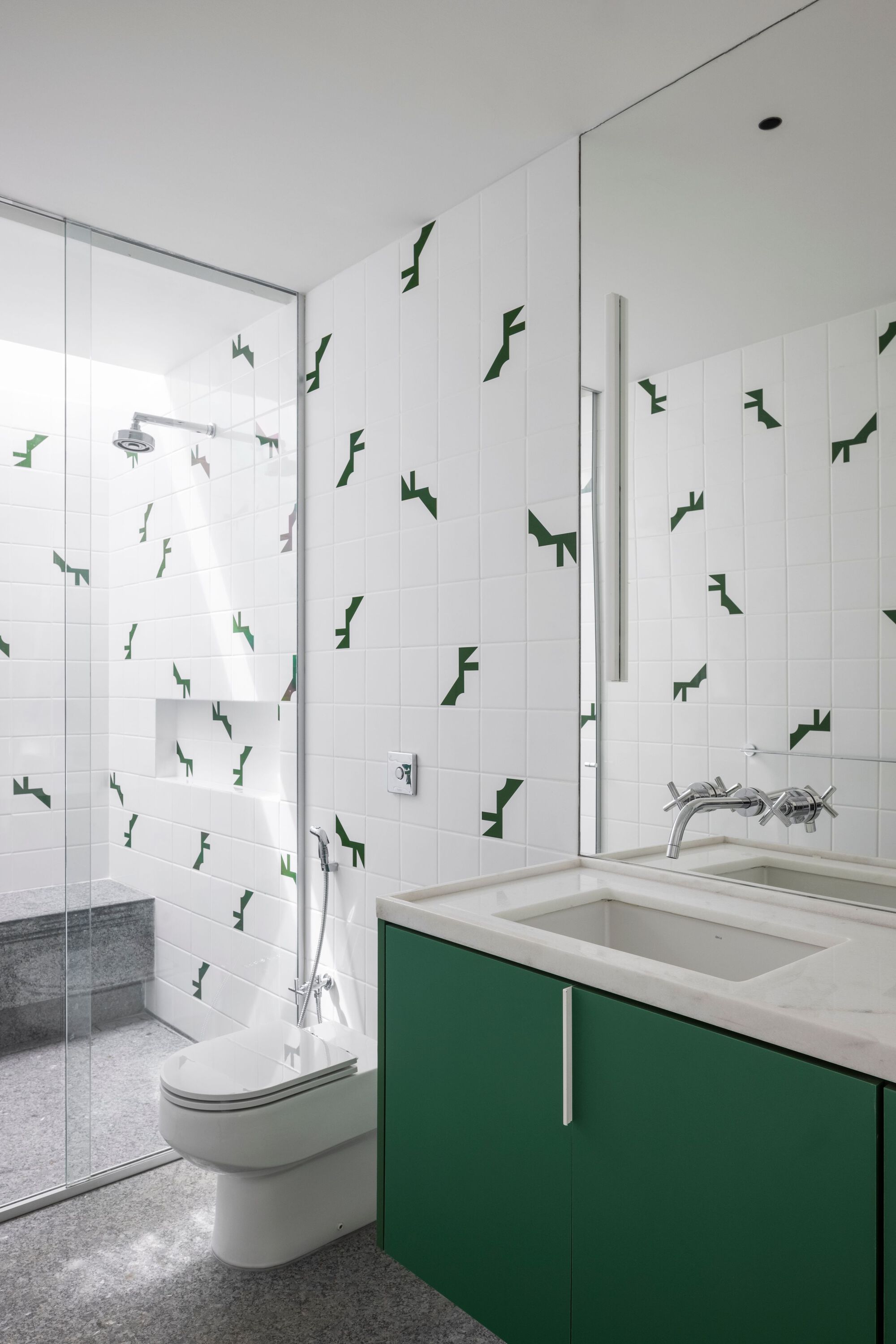 Bathroom with green vanity cabinetry, white tiled walls decorated with dark green geometric decals, and terrazzo flooring